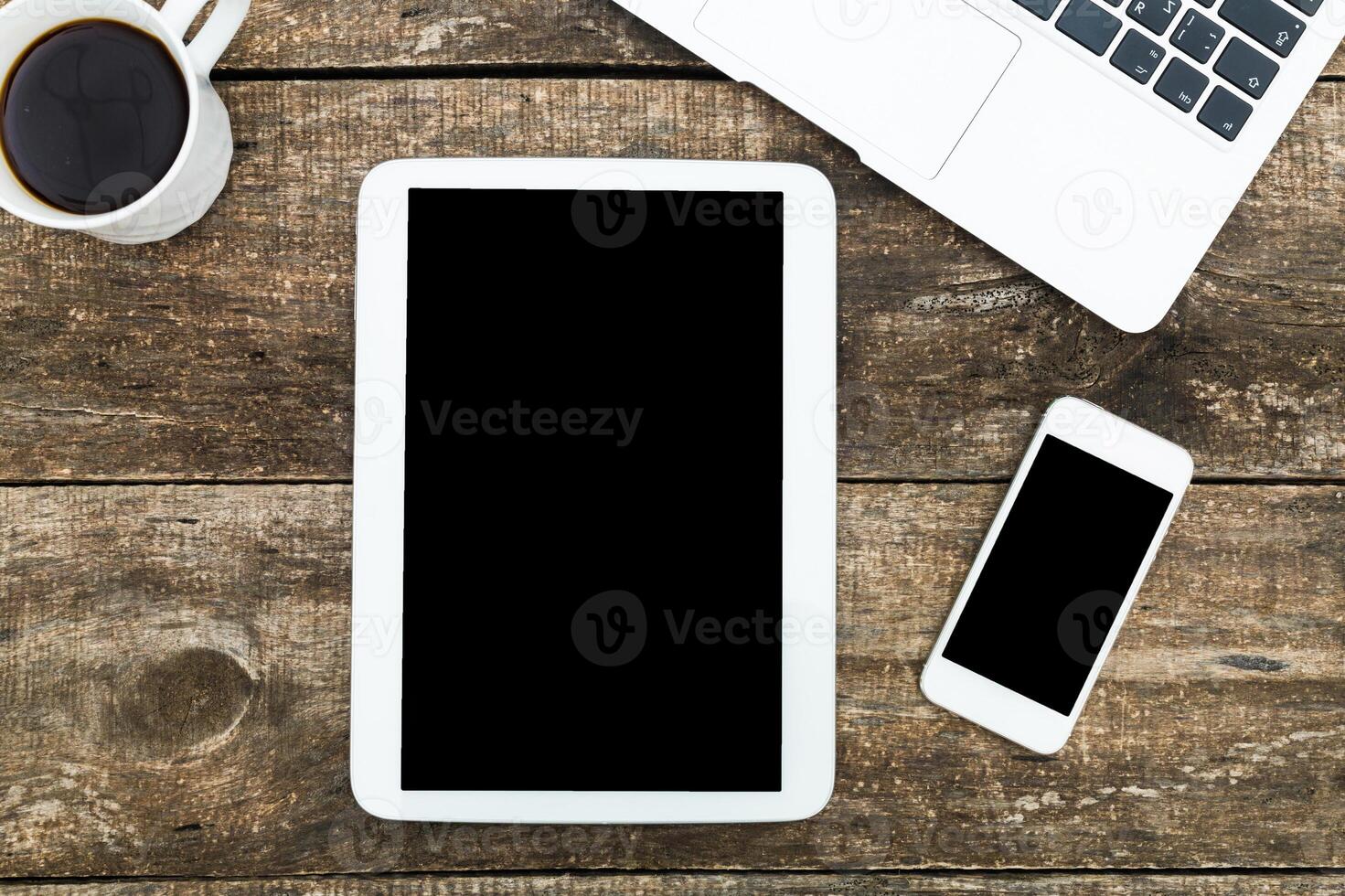 Desk setup featuring tablet, smartphone, laptop, and coffee cup on rustic wooden surface during daytime photo