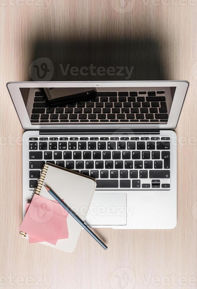 Workspace setup featuring a laptop, notepad, and stationery on a wooden table during daytime photo
