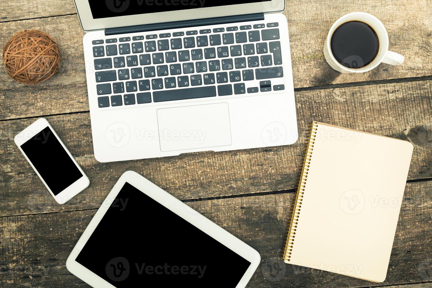 Workspace setup featuring laptop, tablet, smartphone, coffee cup, and notepad on wooden table photo