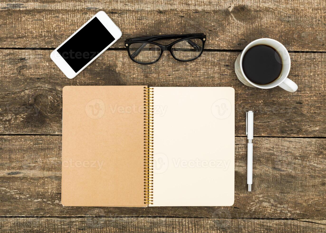 Workspace setup with notebook, pen, coffee, smartphone, and glasses arranged on wooden table photo