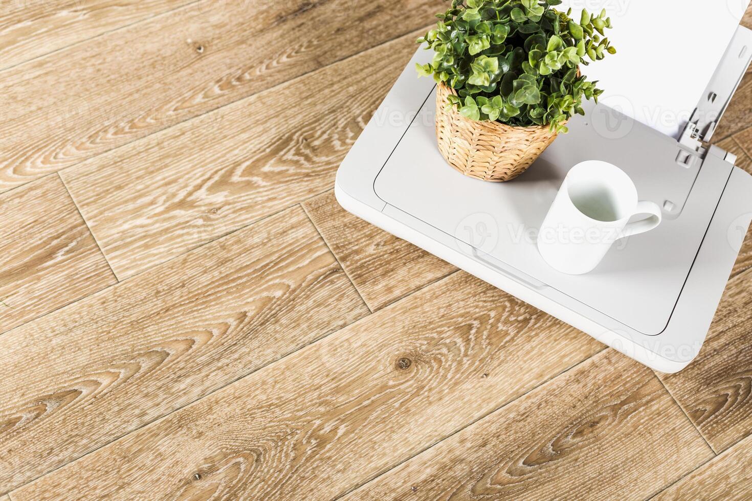 Modern workspace setup with wooden flooring, plant, and coffee cup on a table in natural light photo