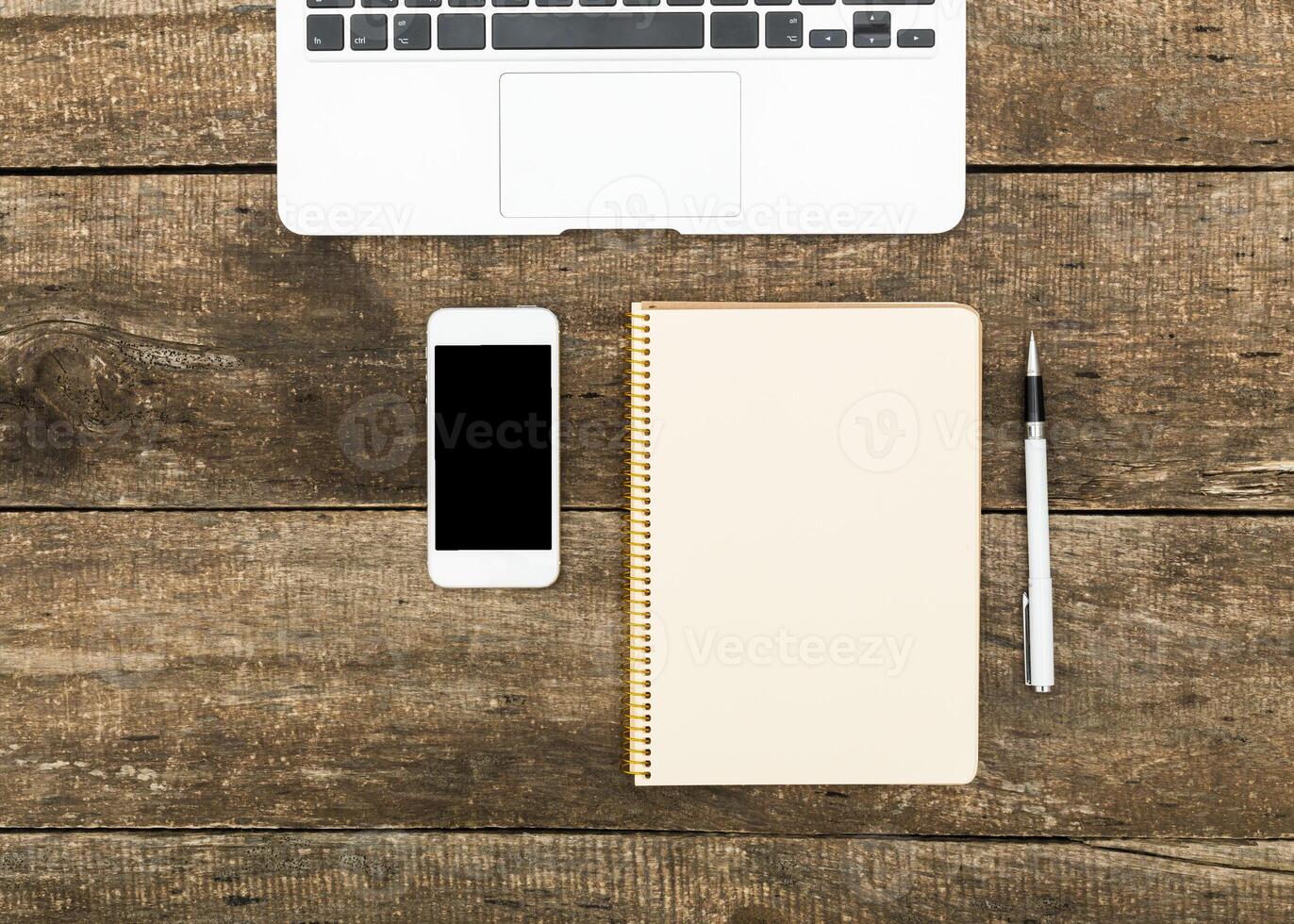 Workspace setup with laptop, smartphone, notepad, and pen on rustic wood table for productivity photo