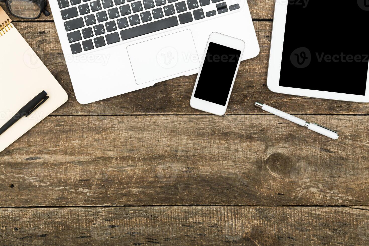 Workspace with laptop, smartphone, tablet, and stationery on wooden table during daylight hours photo