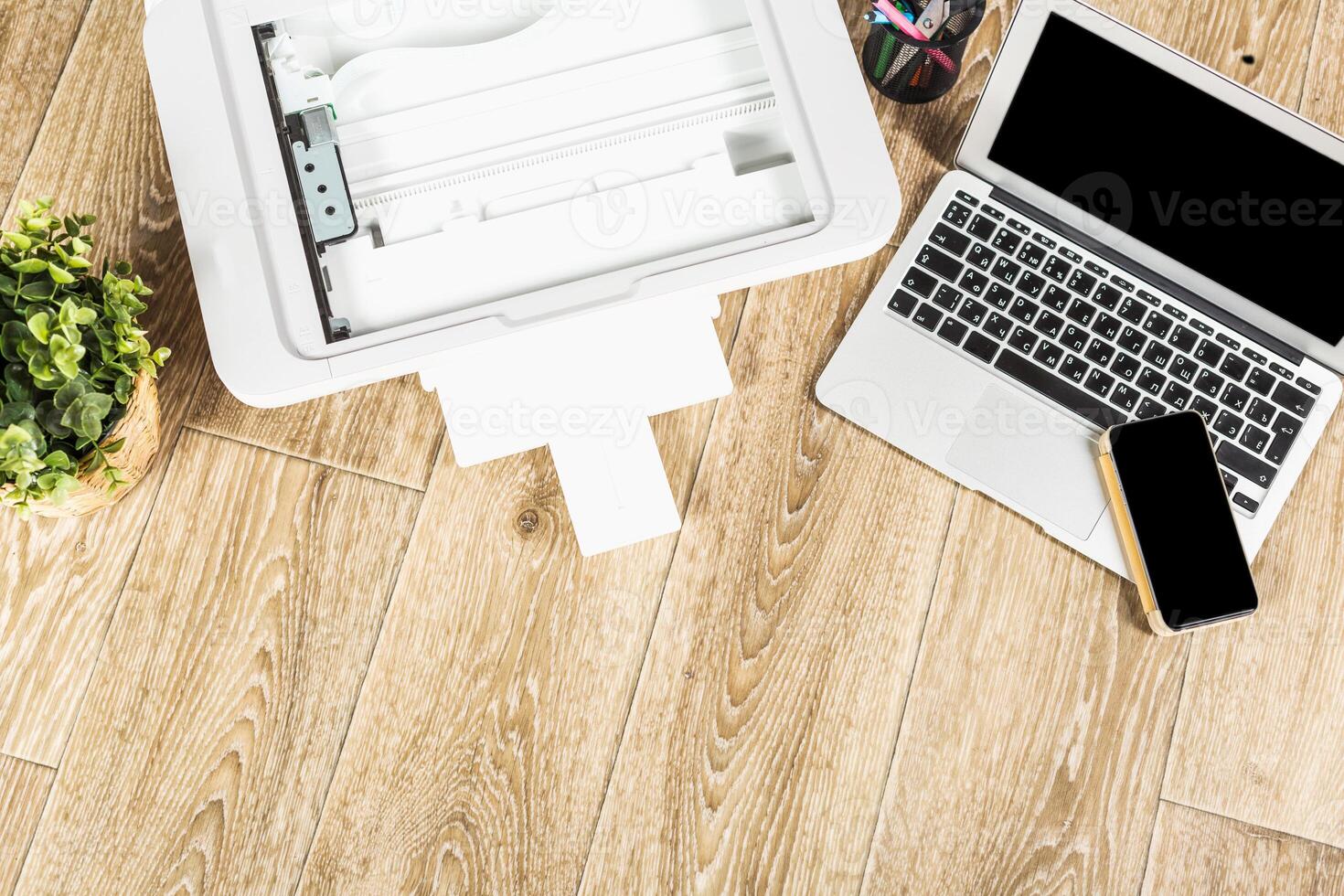 Working environment with a laptop, printer, and smartphone on a wooden desk during the day photo