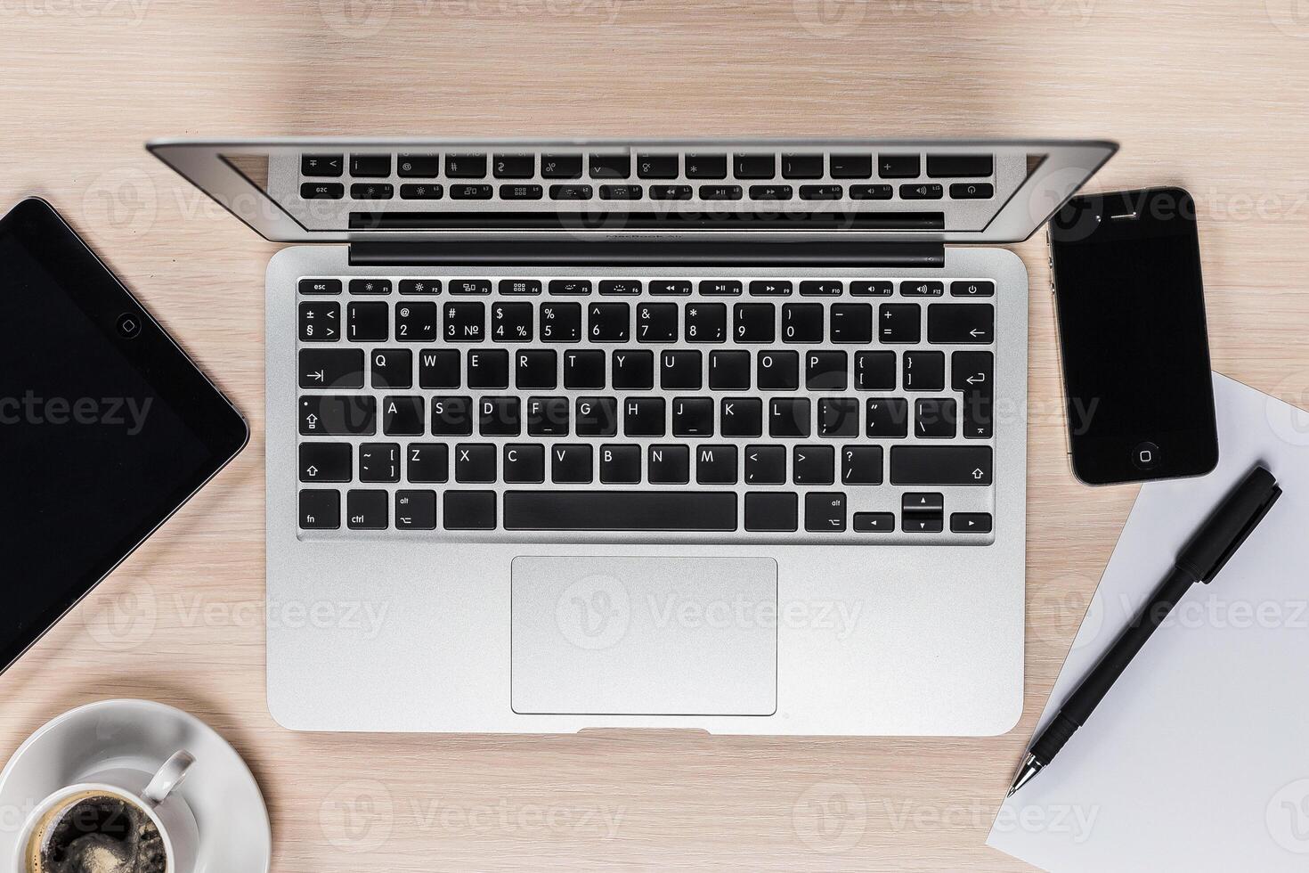 Workspace setup featuring a laptop, mobile devices, coffee, and stationery on a wooden table photo