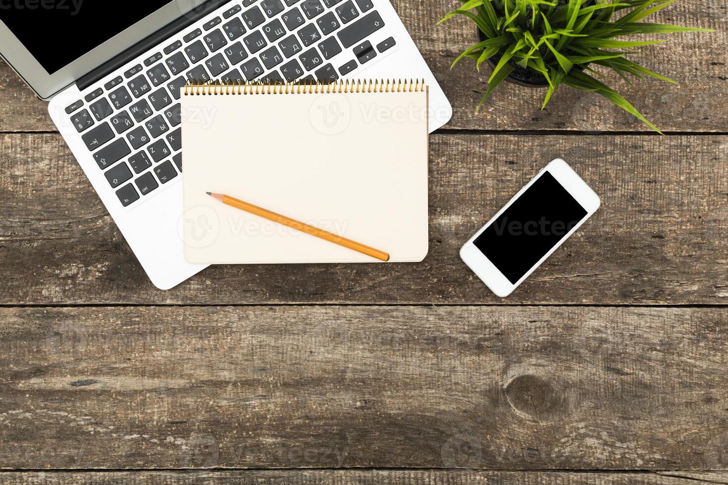 Workspace setup with laptop, smartphone, notepad, and pencil on wooden table during daytime photo