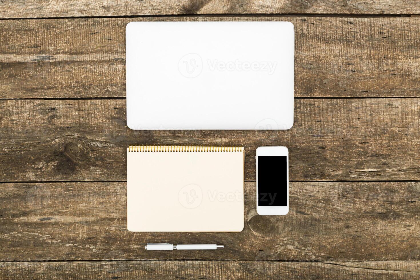 Workspace setup featuring a laptop, notebook, phone, and pen on a wooden table photo