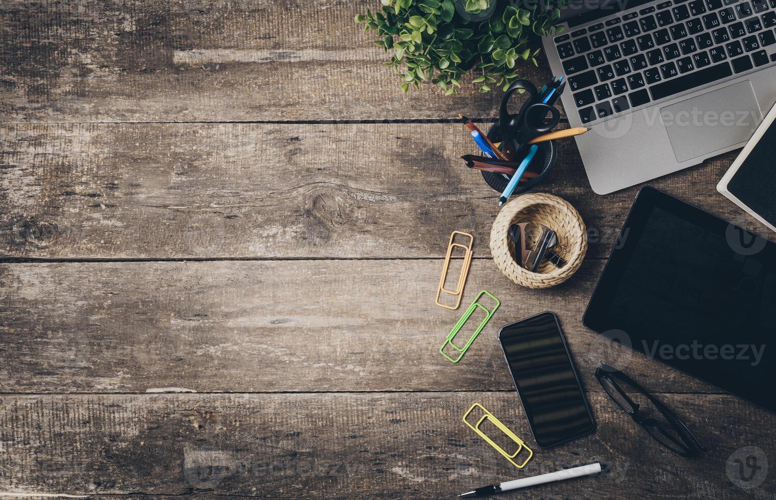 Workspace setup featuring laptop, tablet, smartphone, and stationary items on rustic wooden table photo