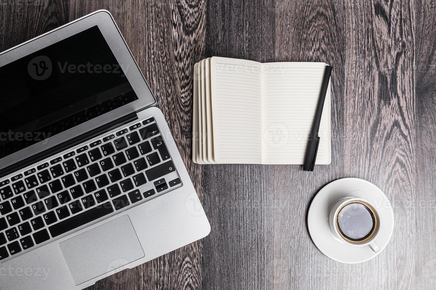 Workspace with laptop, notebook, pen, and coffee cup on wooden table during a quiet morning photo