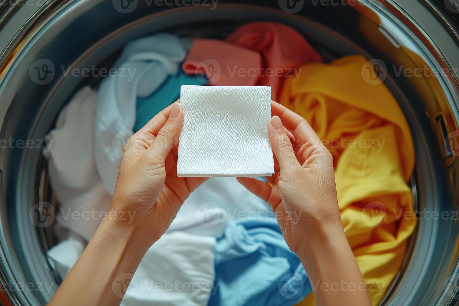 Hands holding fabric softener sheet above laundry.. photo
