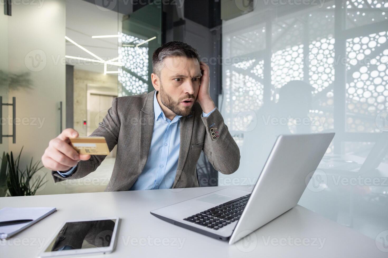 Man looking worried while shopping online with a credit card in a modern office, expressing concern about an online transaction photo