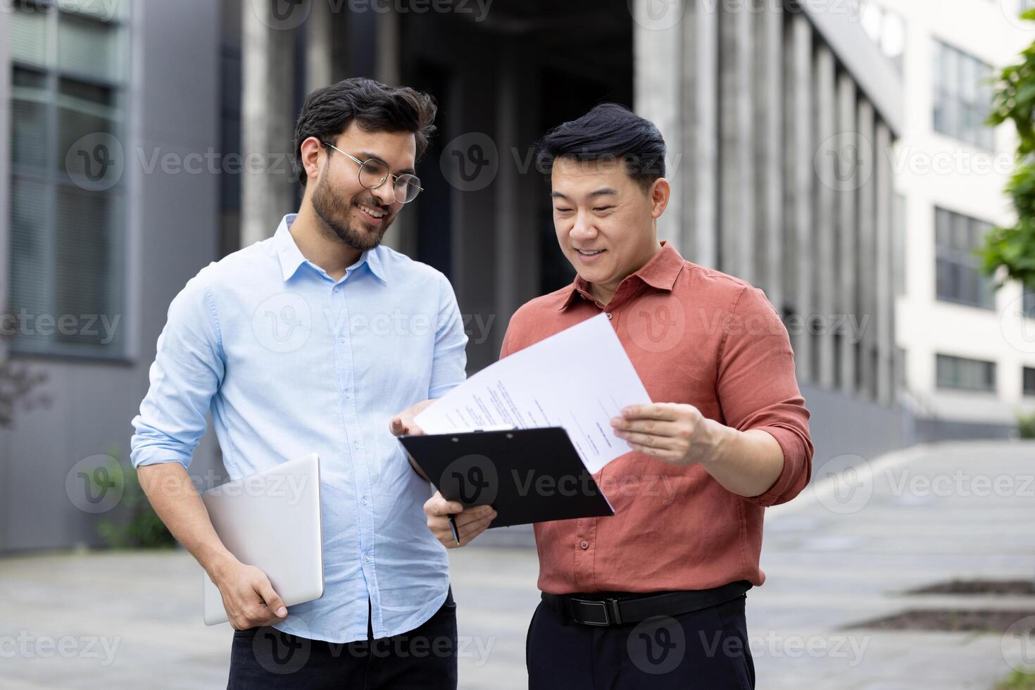 Two colleagues of office company employees discussing financial reports, contracts and documents, group of business people outside office building with papers in hands discussing. photo