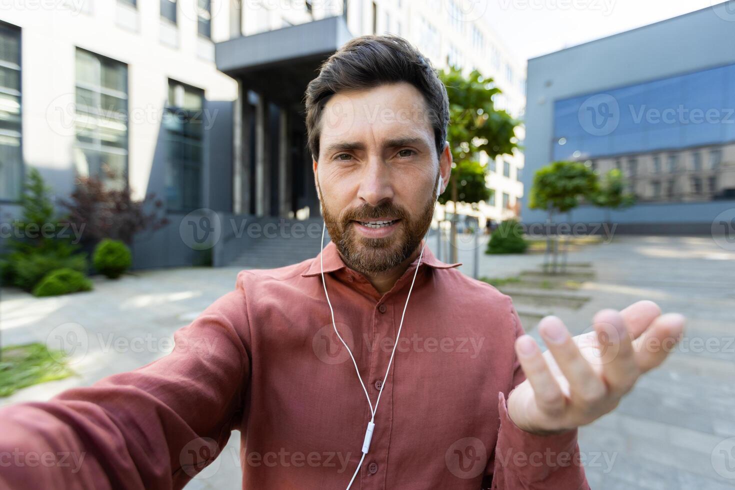 Man with headphones looking into phone camera. Office worker businessman talking to colleagues and friends walking around the city using call, smartphone app. photo