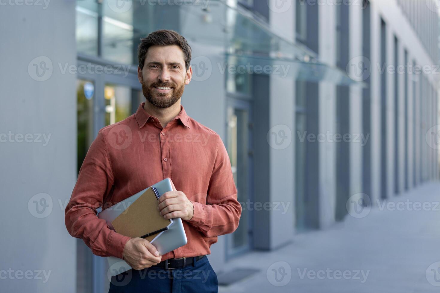 Professional businessman smiling outside urban office holding tablet and notebook. Confident expression, casual attire. Ideal for business, career advancement, confidence themes. photo