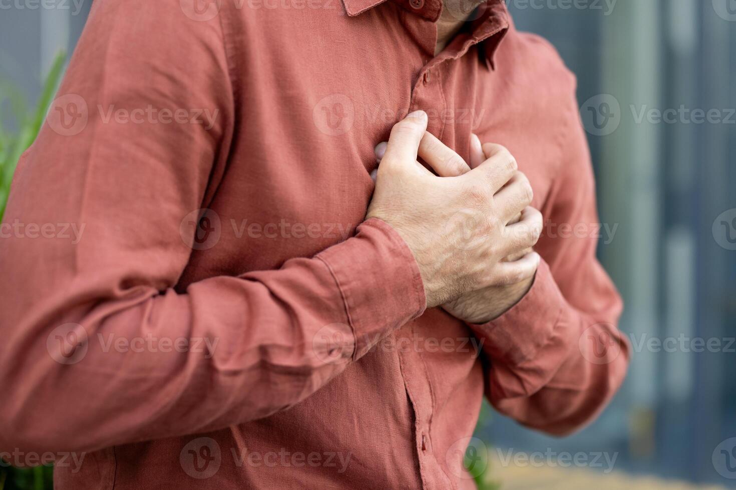 Person holding chest in rust-colored shirt signifies pain, stress, or heart-related concern. Close-up emphasizes emotion and tension in hands. Suitable for health or wellness themes. photo