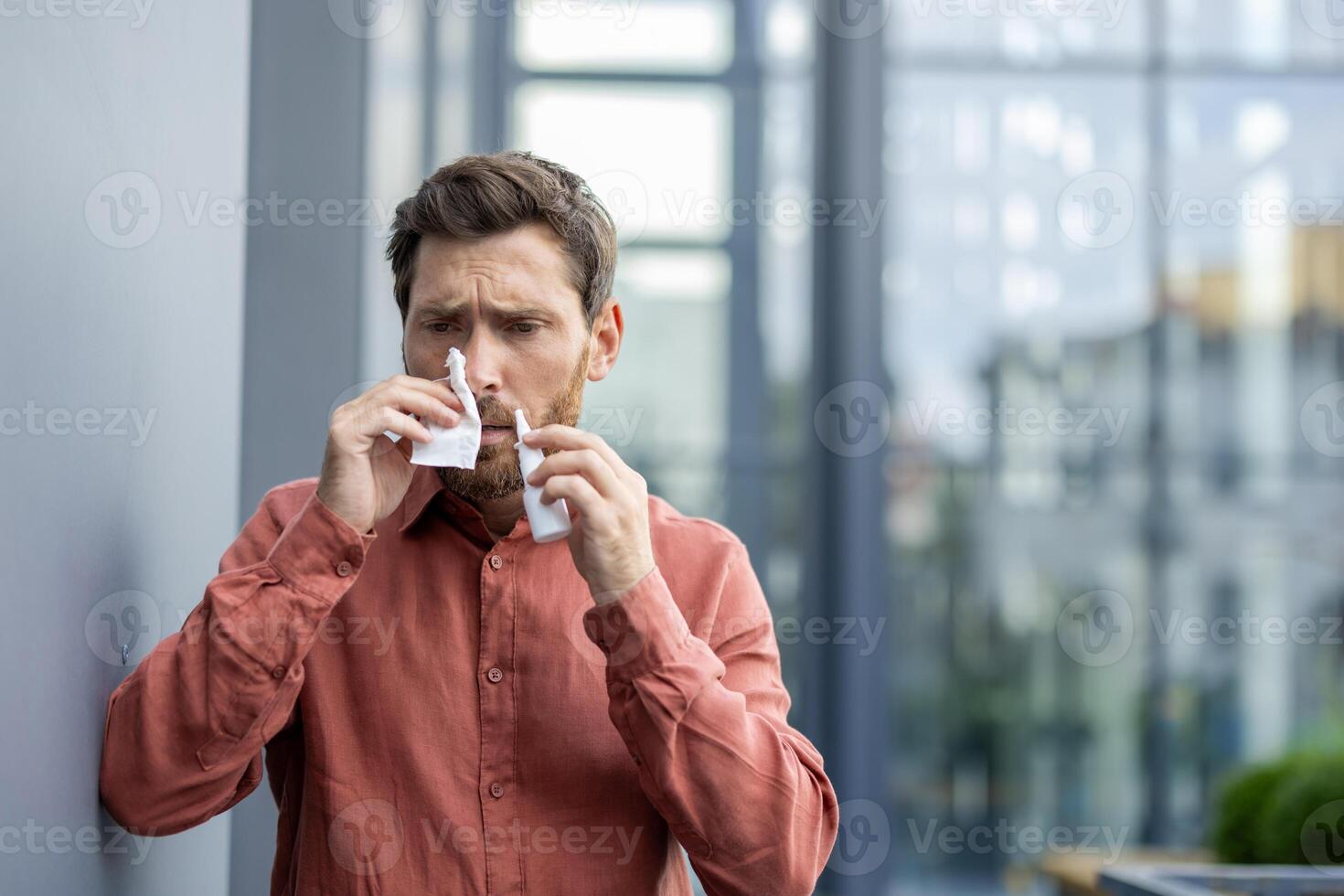 Man using tissue outdoors in urban setting, wearing casual shirt, looking concerned. Scene depicts health issues like cold or allergies, reflecting everyday challenges in wellness and hygiene. photo