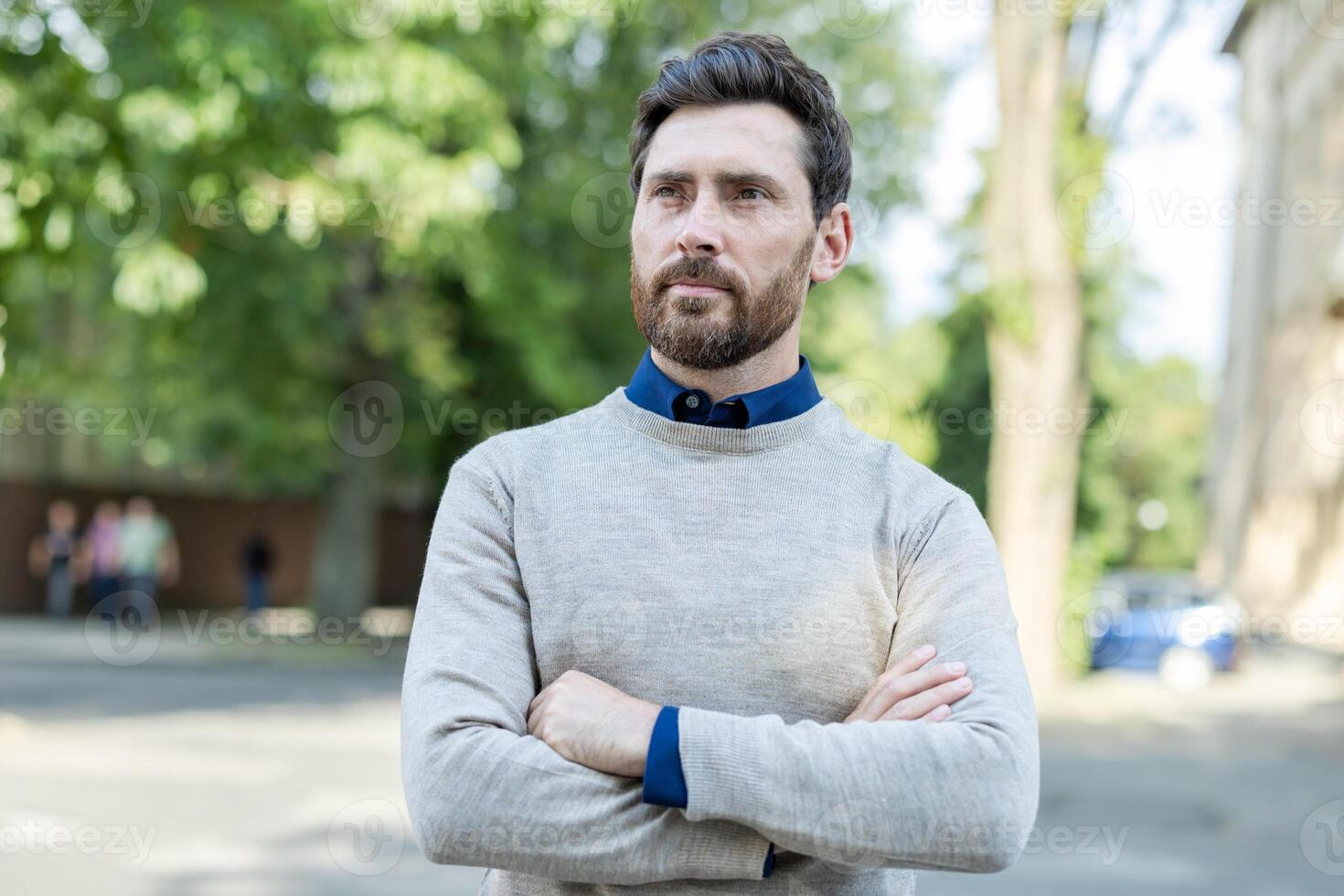 Confident adult male professional standing with arms crossed on urban street. Mature businessman exudes leadership and focus, dressed in casual attire. Outdoors setting highlights city environment photo