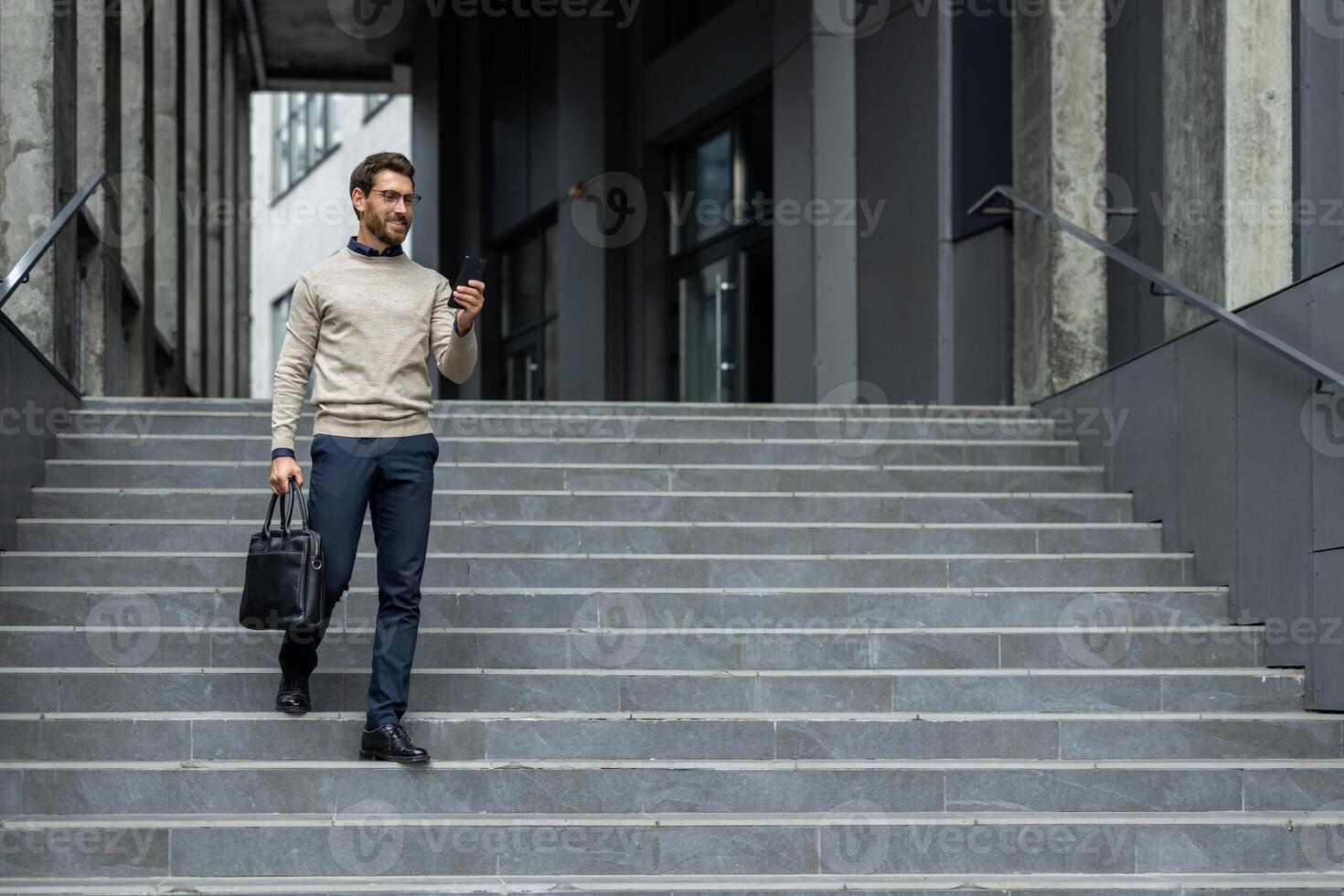 Serious man descends stairs in city while using phone. He wears business attire and carries leather briefcase, exhibiting focused and professional demeanor. photo