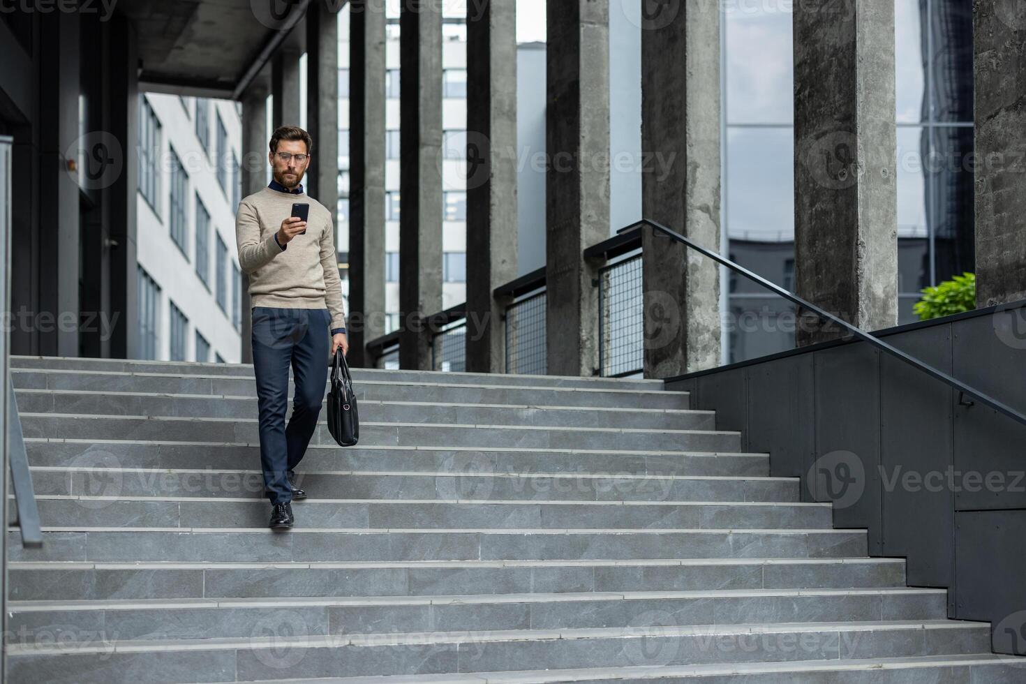 Businessman descends urban stairs while focused on smartphone, demonstrating modern professional life. Dressed in casual business attire, he efficiently multitasks between phone photo