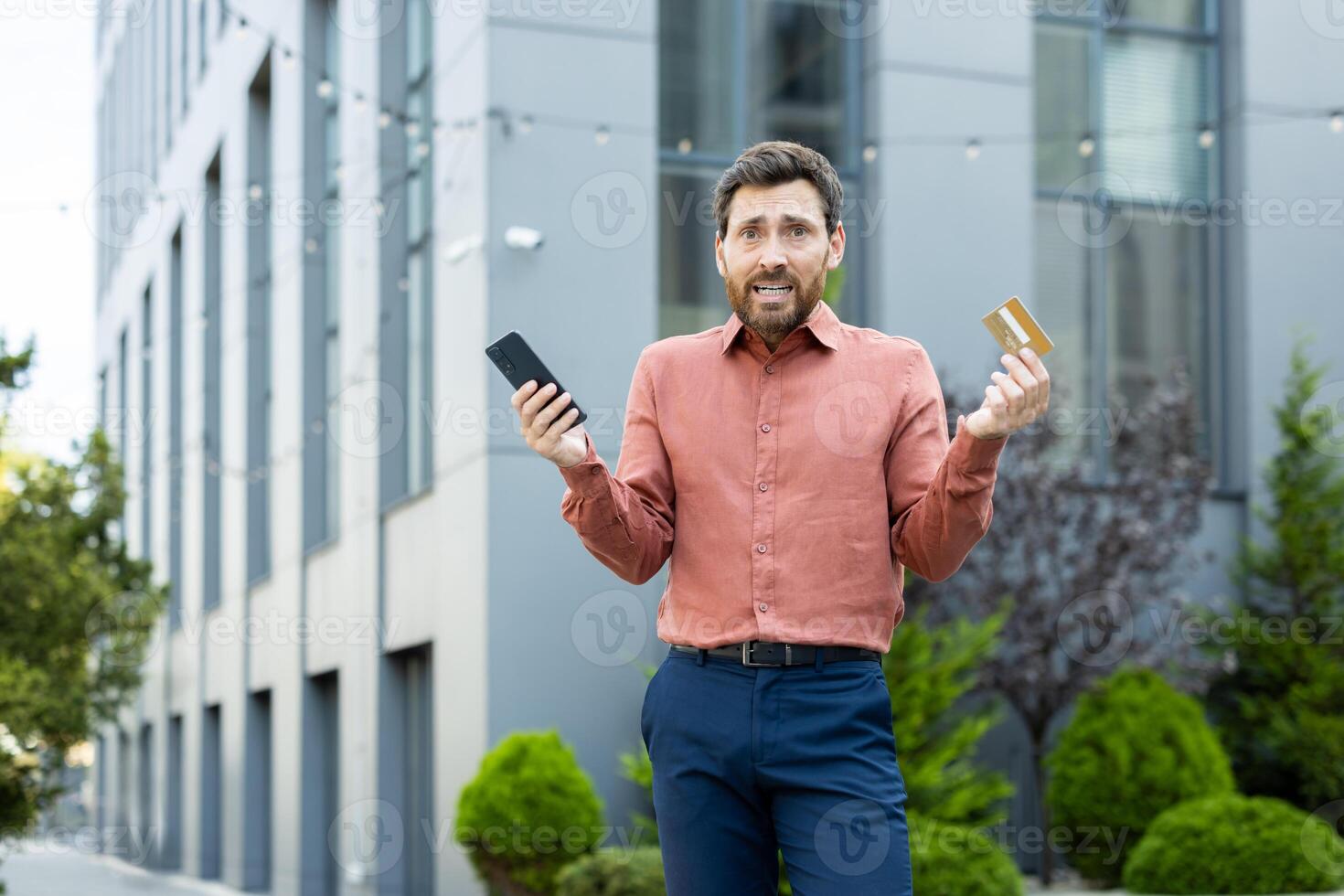 Portrait of a deceived and disappointed man, holding a bank credit card and phone in his hands, account blocked, and money transfer error photo