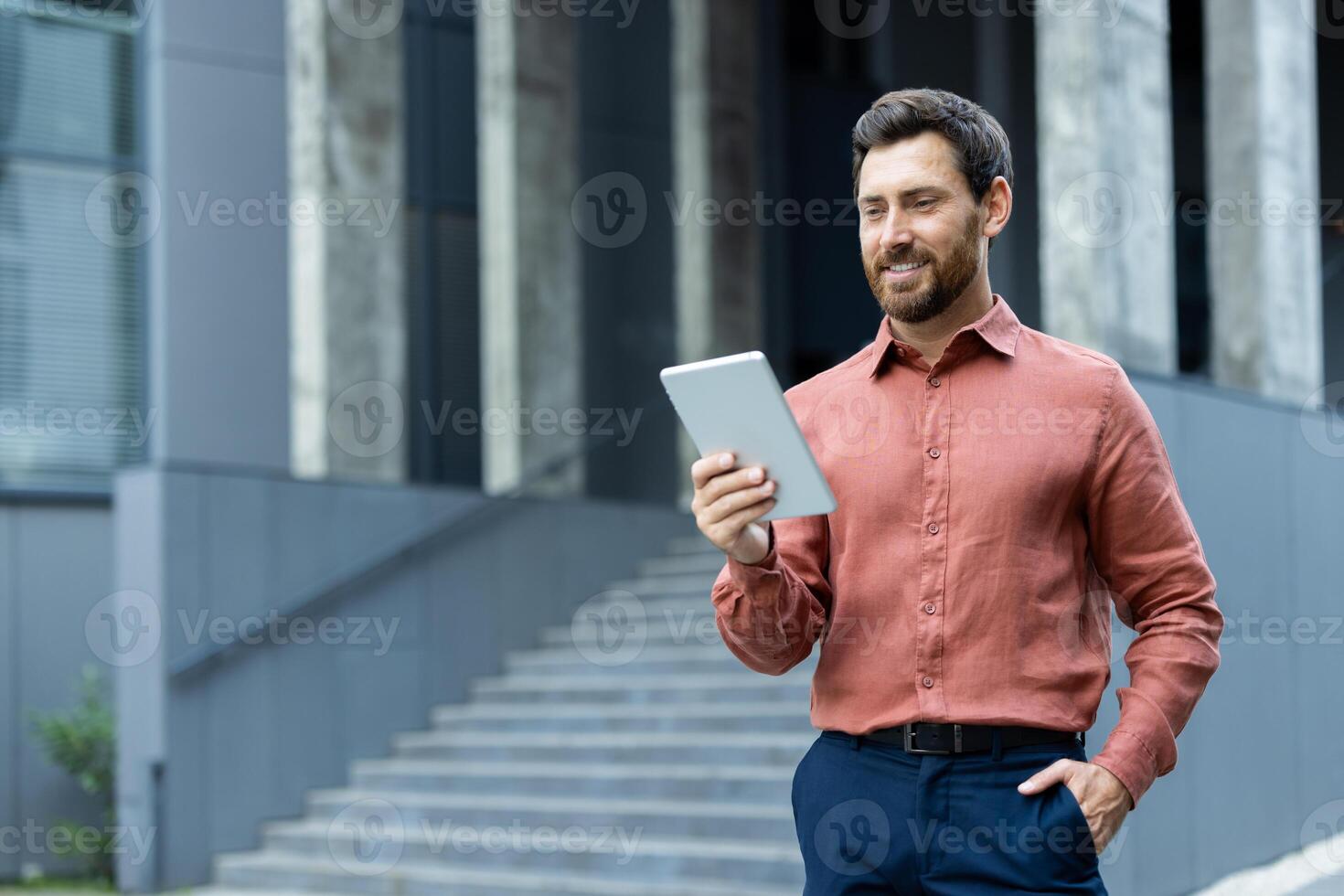 A confident man is using a tablet outside a striking modern building, which showcases a strong professional vibe. photo