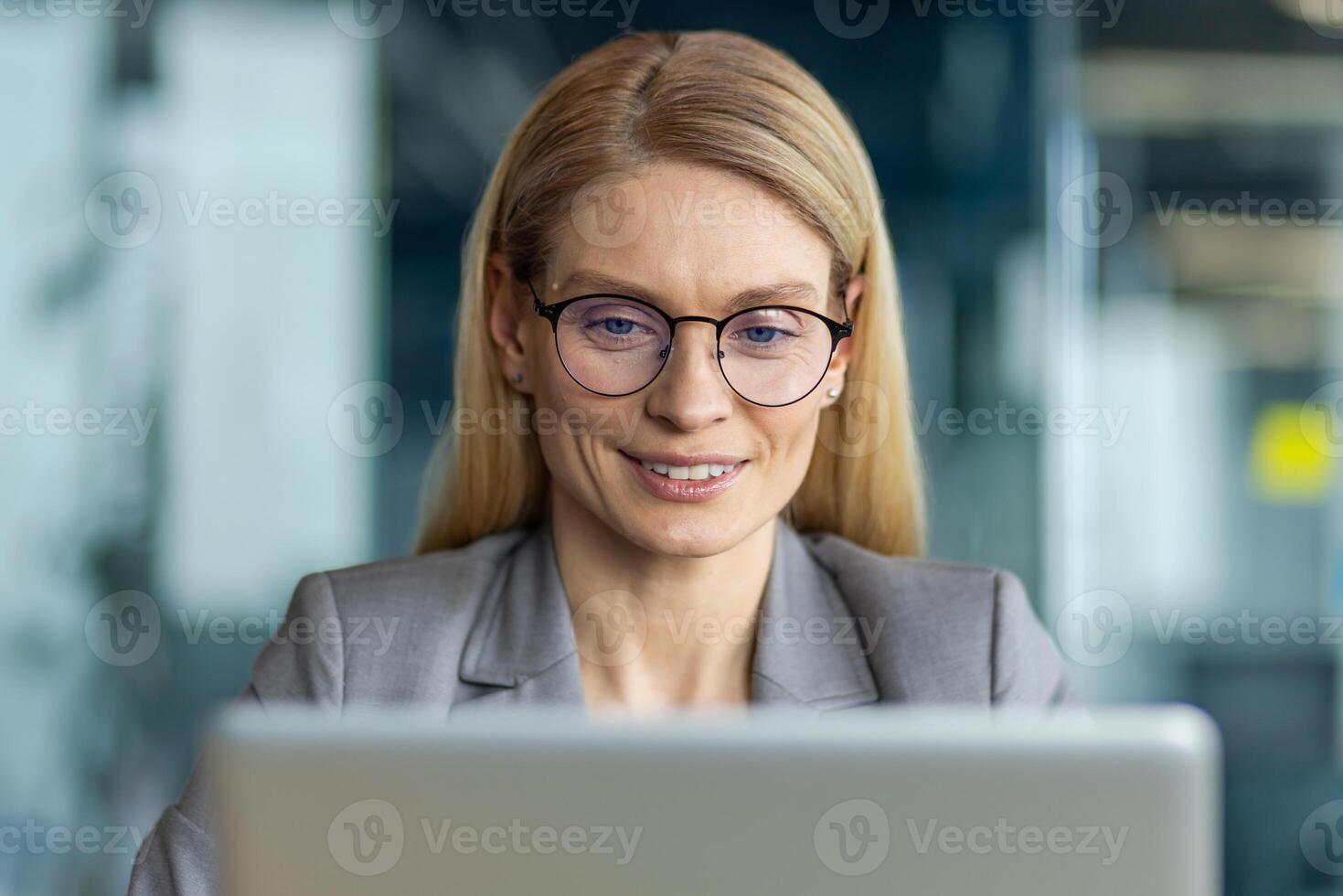 Confident businesswoman wearing glasses focused on working with laptop in modern office. Demonstrates professionalism and concentration while engaging with digital work environment photo
