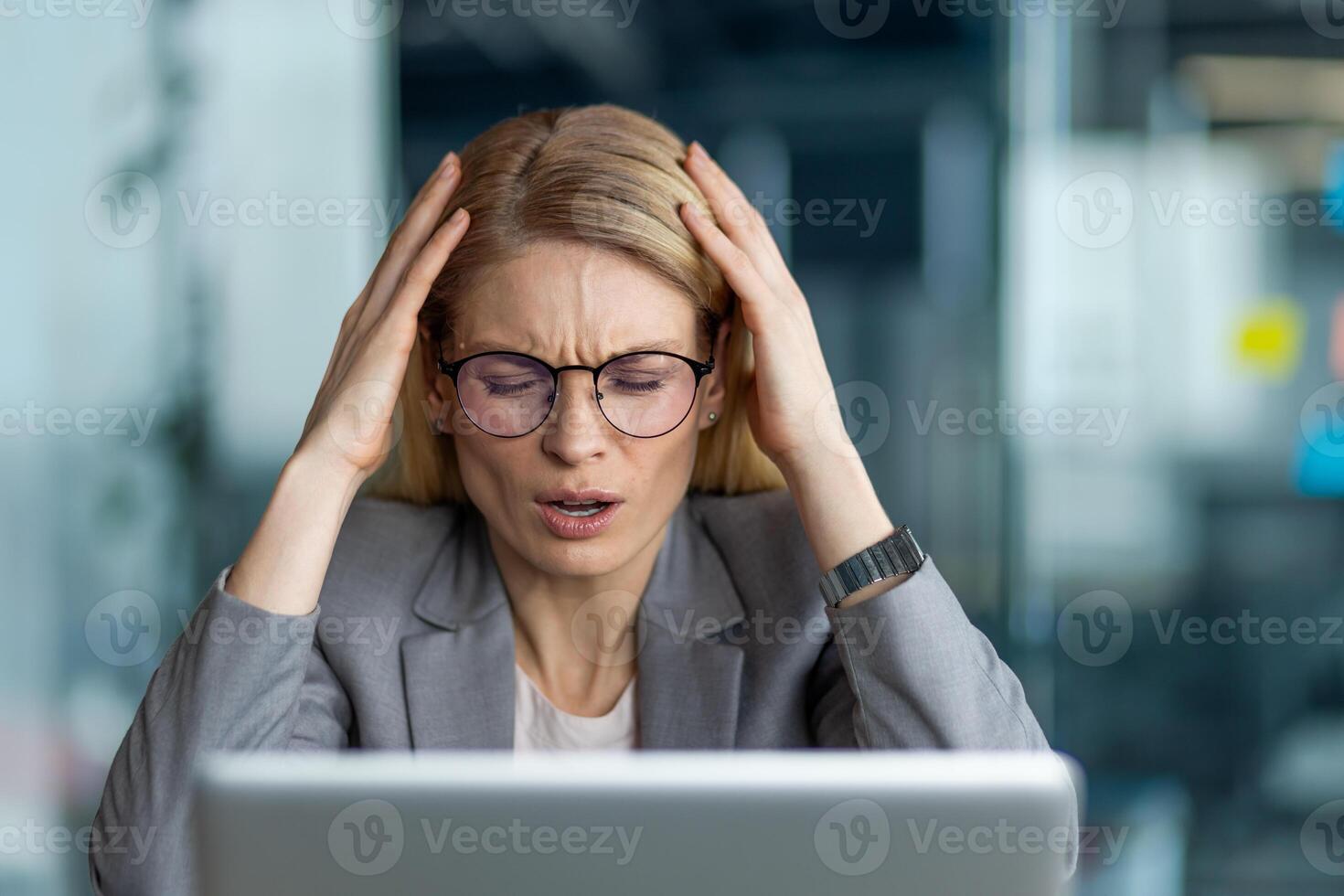 Businesswoman wearing glasses feeling stressed and frustrated while working in office setting. Woman expresses anxiety and pressure in professional environment. Concept of stress management photo