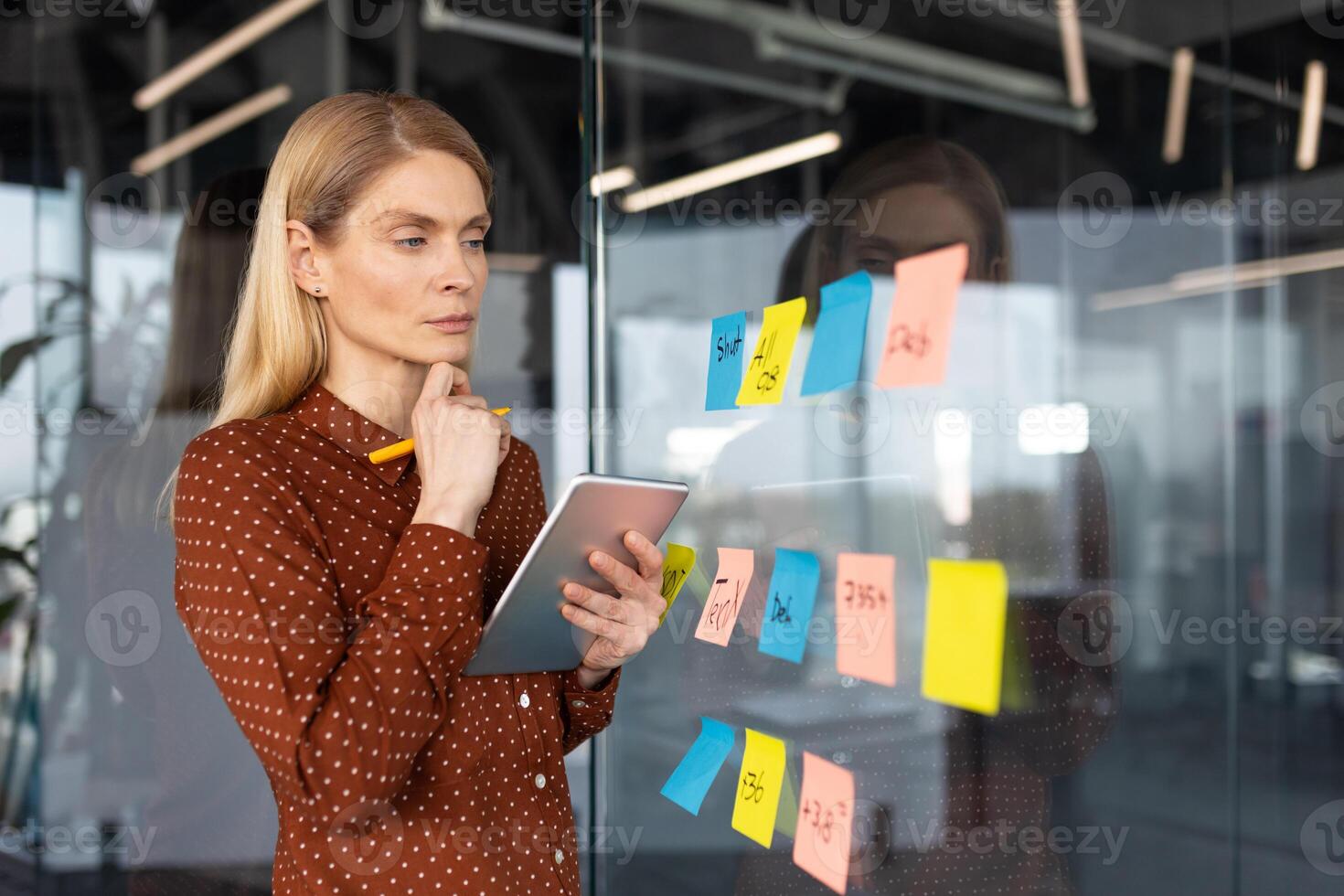 Focused businesswoman using sticky notes for brainstorming and planning on a glass wall in a modern office setting. photo