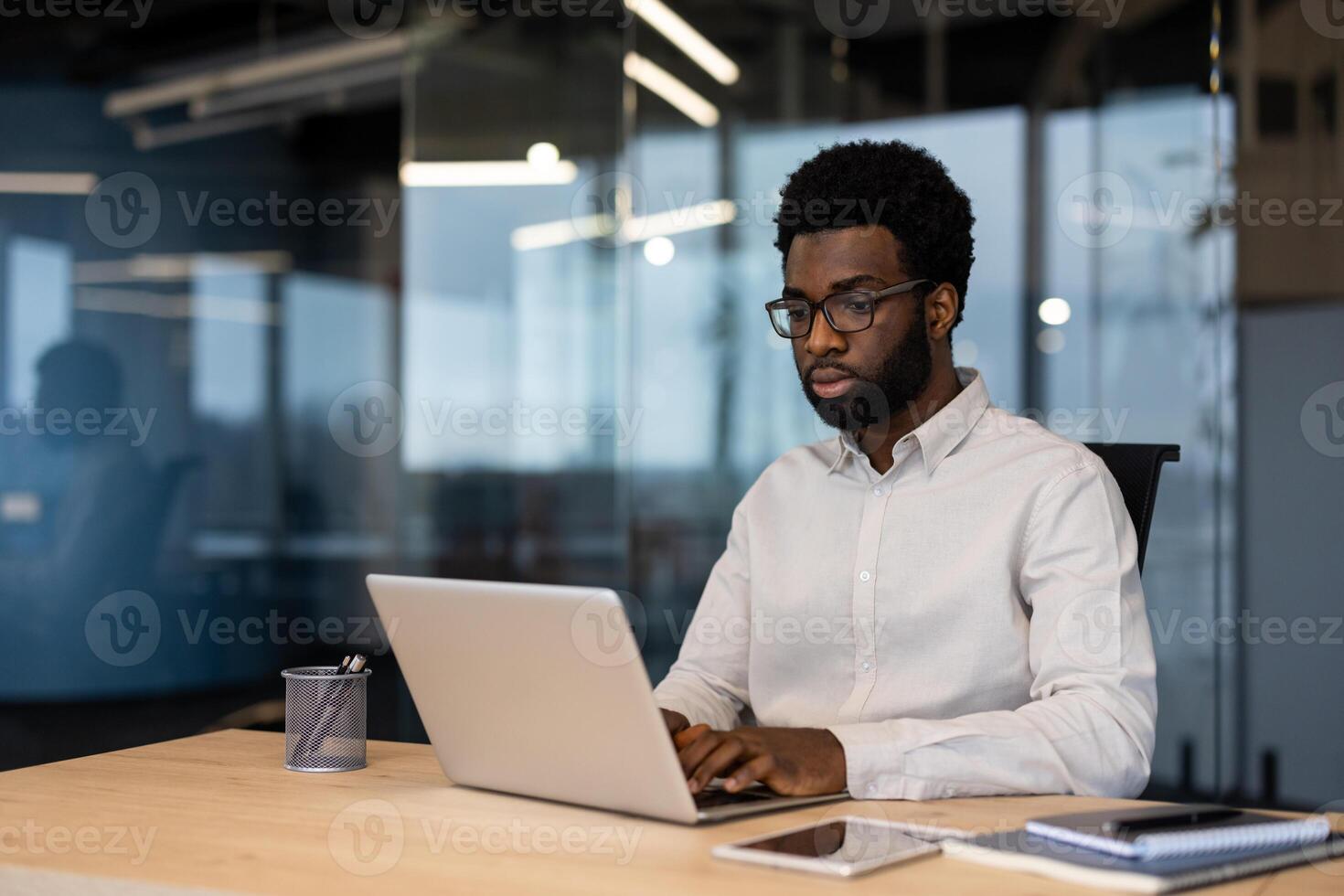 Serious thinking man working inside office with laptop, businessman in shirt typing on computer keyboard, working in evening at work. photo