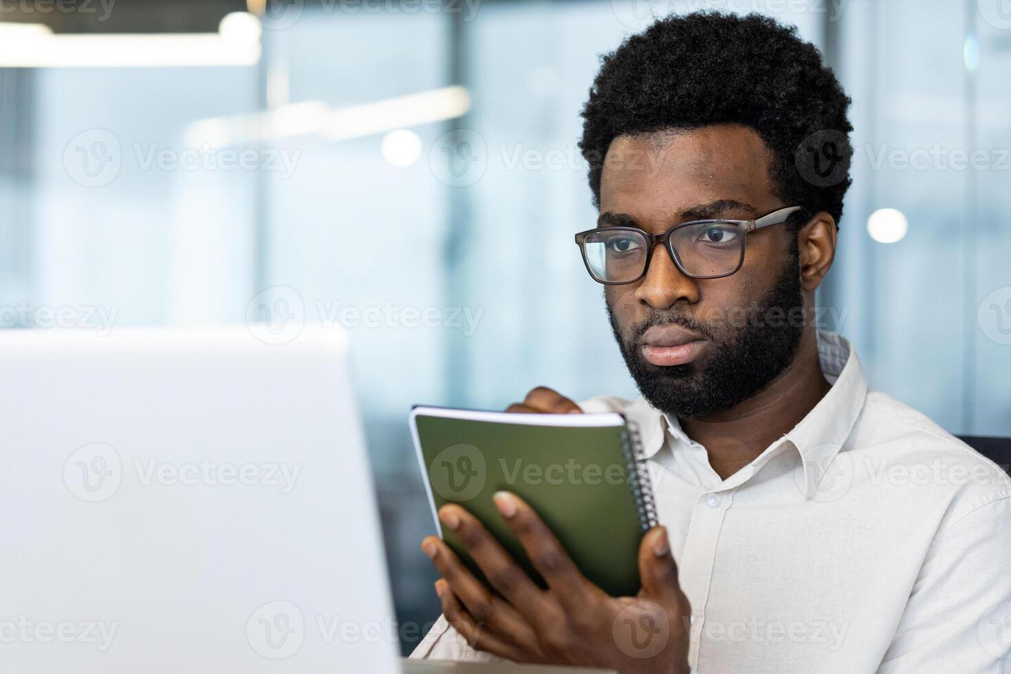 Business meeting online conference, man close up with notepad writing down data and studying remotely sitting inside office with laptop, businessman watching webinar online broadcast. photo
