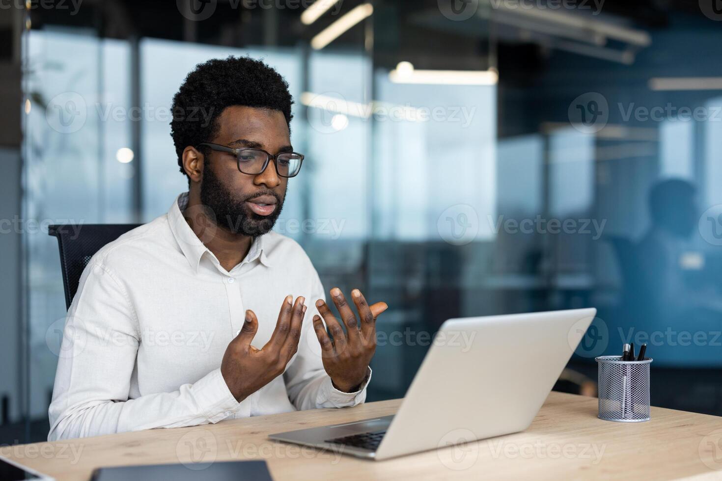 Serious focused man talking to colleagues and partners remotely using laptop and call. Promising businessman on online conference meeting inside office. photo