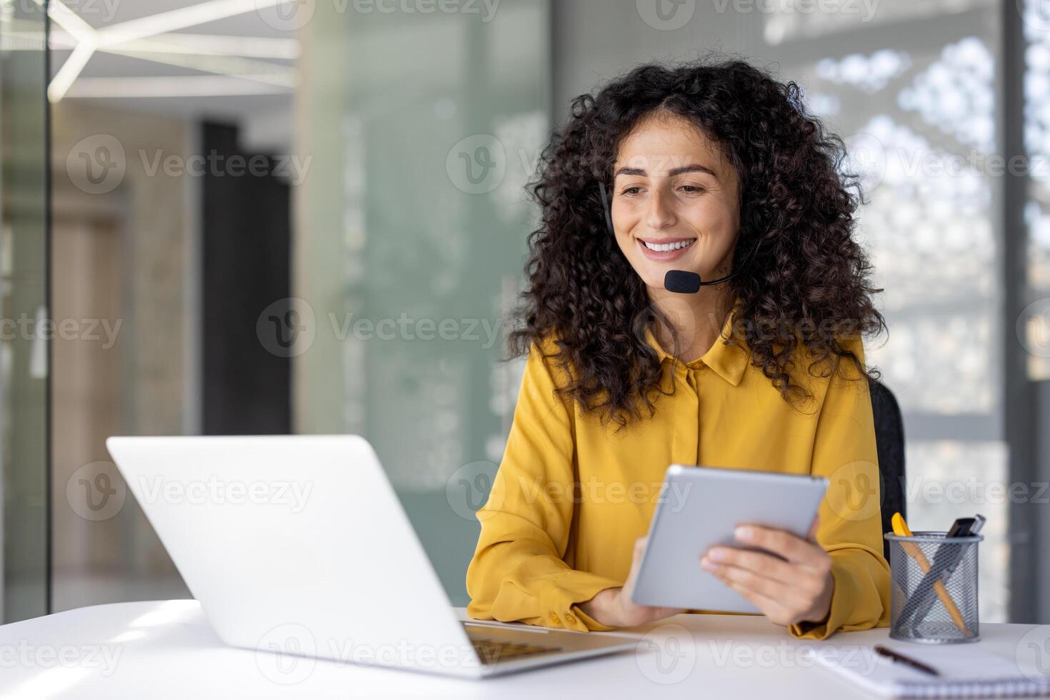 Woman with headset at workplace inside office holding tablet computer. Office worker of customer support and consulting service, inside office at workplace with laptop. photo