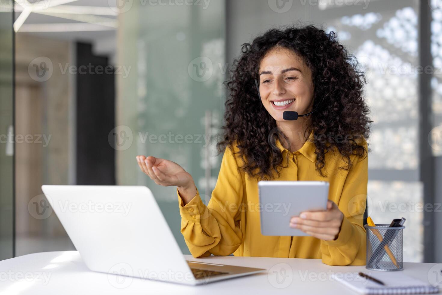 Support service worker, businesswoman with headset and tablet in hands communicates and consults clients remotely, office worker smiles satisfied uses laptop inside office. photo