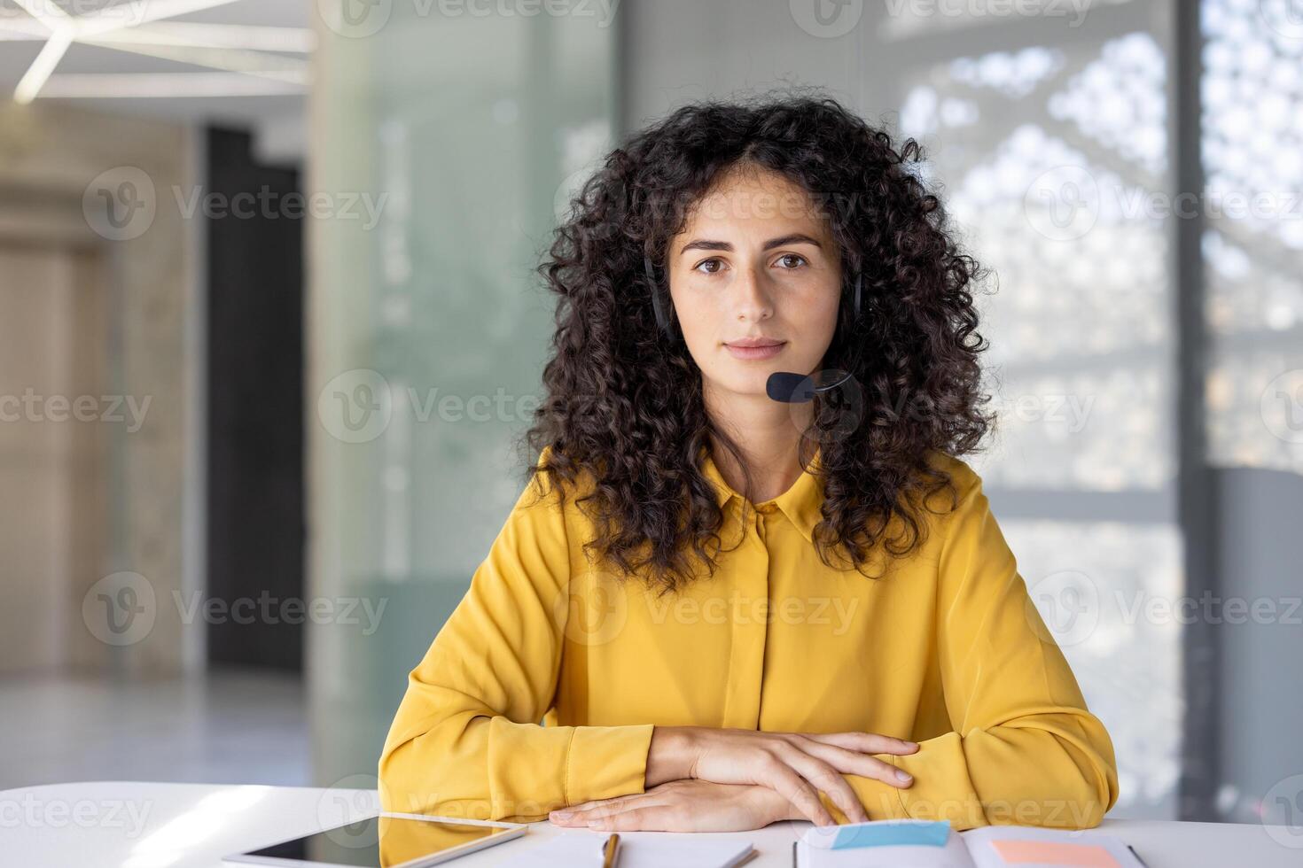 Serious woman listening to conversation while sitting with headset. Office worker looking at camera with concentration, online call, business meeting, remote conference. photo