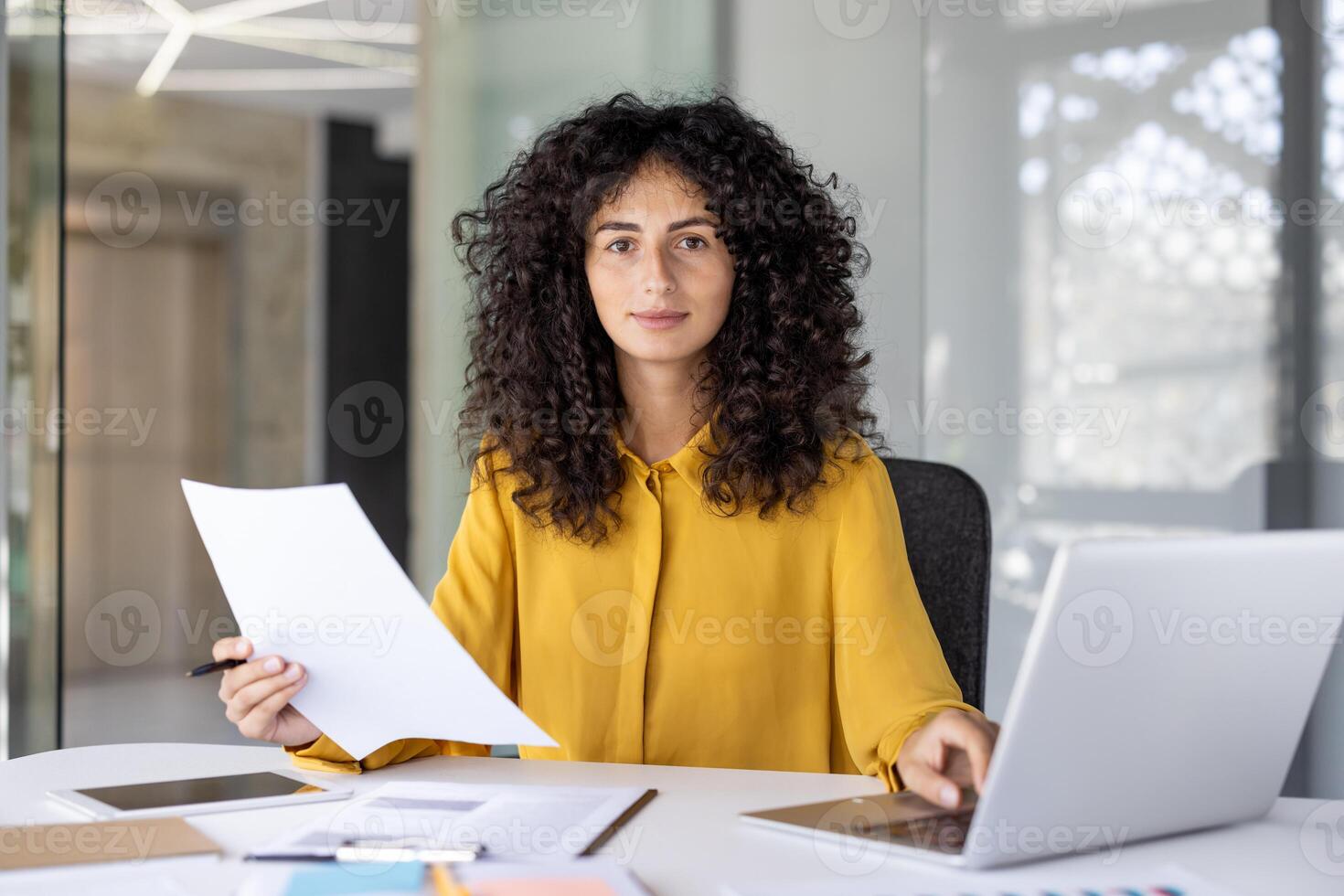 Portrait of serious focused woman doing paperwork inside office, businesswoman looking thoughtfully at camera, working with contracts and financial reports. photo