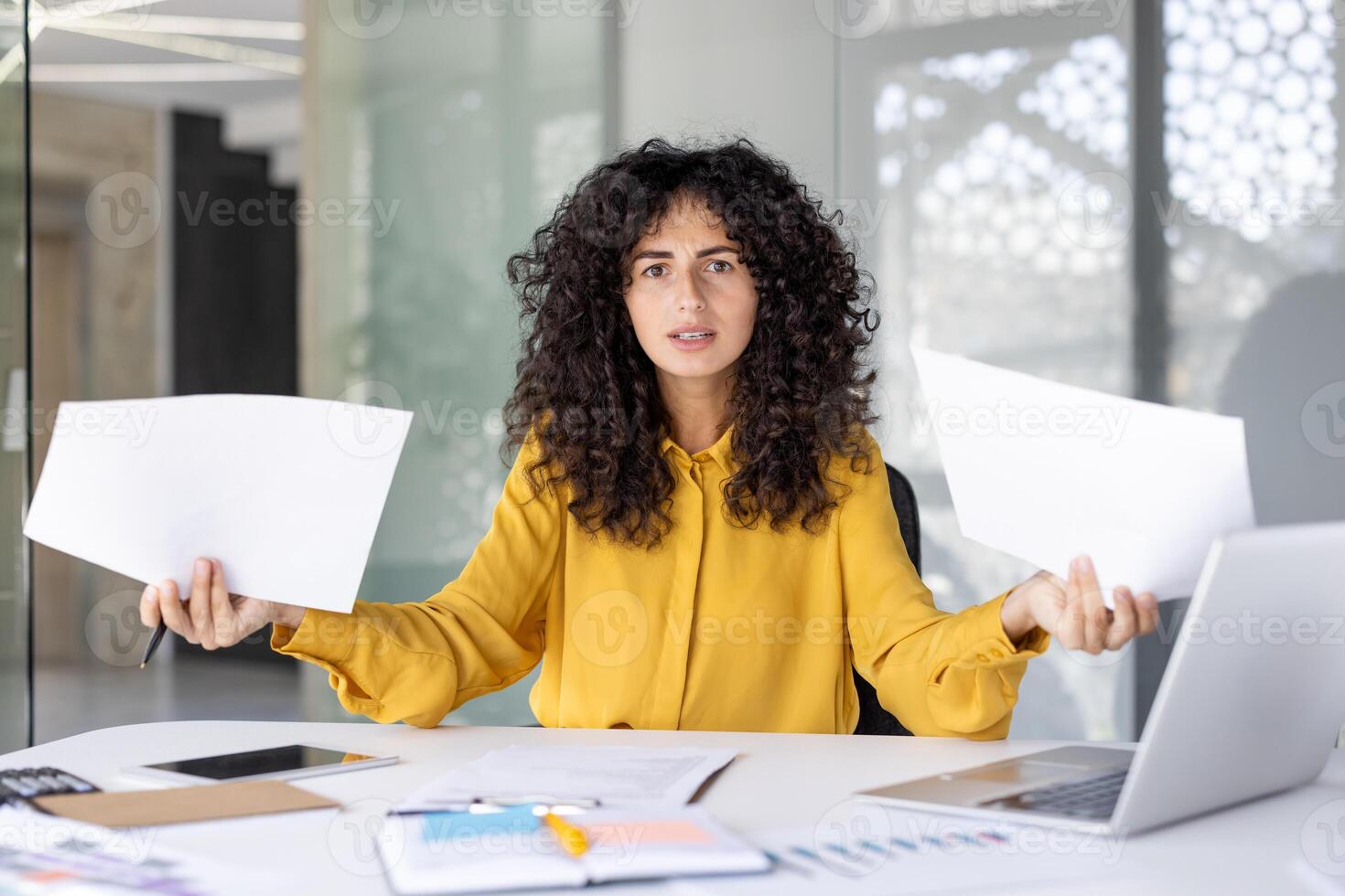 Portrait of confused and disappointed woman at workplace with papers and documents in hands. Financier looking at camera dissatisfied with achievements, bad reports. photo
