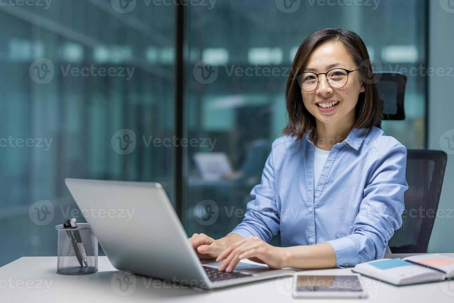 Portrait of a young successful Asian businesswoman, office worker smiling and looking at the camera, woman at workplace inside office working with laptop. photo