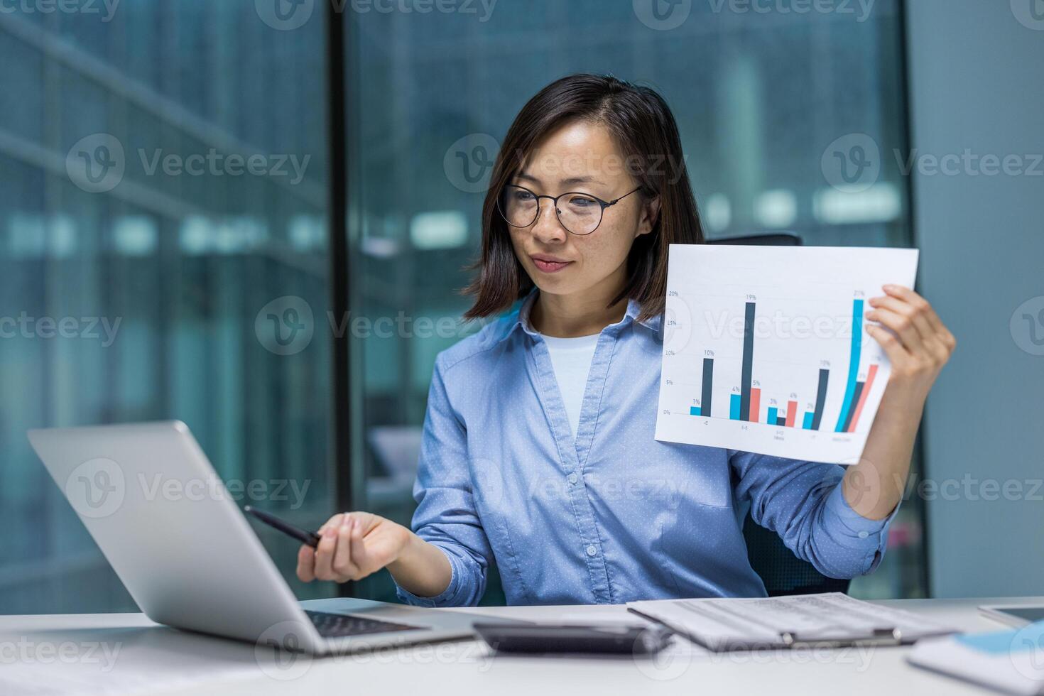 Online presentation, serious focused woman showing company revenue graph into laptop camera, Asian financier explaining key figures, office worker with laptop inside office. photo