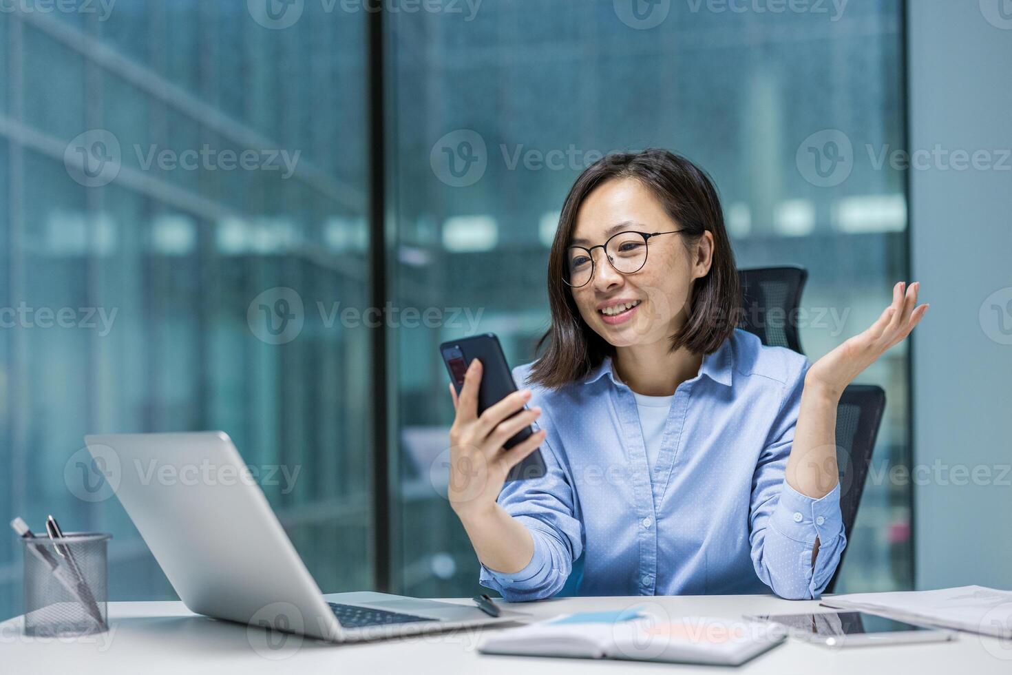 Joyful Asian woman typing message on phone, businesswoman inside office at workplace using app for online communication remotely. photo