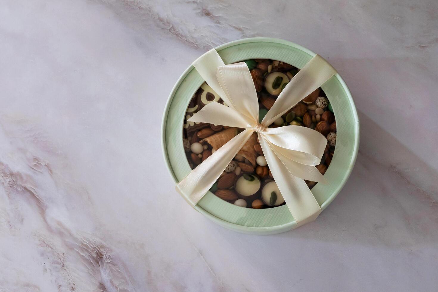 The photograph showcases a diverse selection of treats, from earthy nuts to elegant chocolates and other sweets, contained within a round box photo
