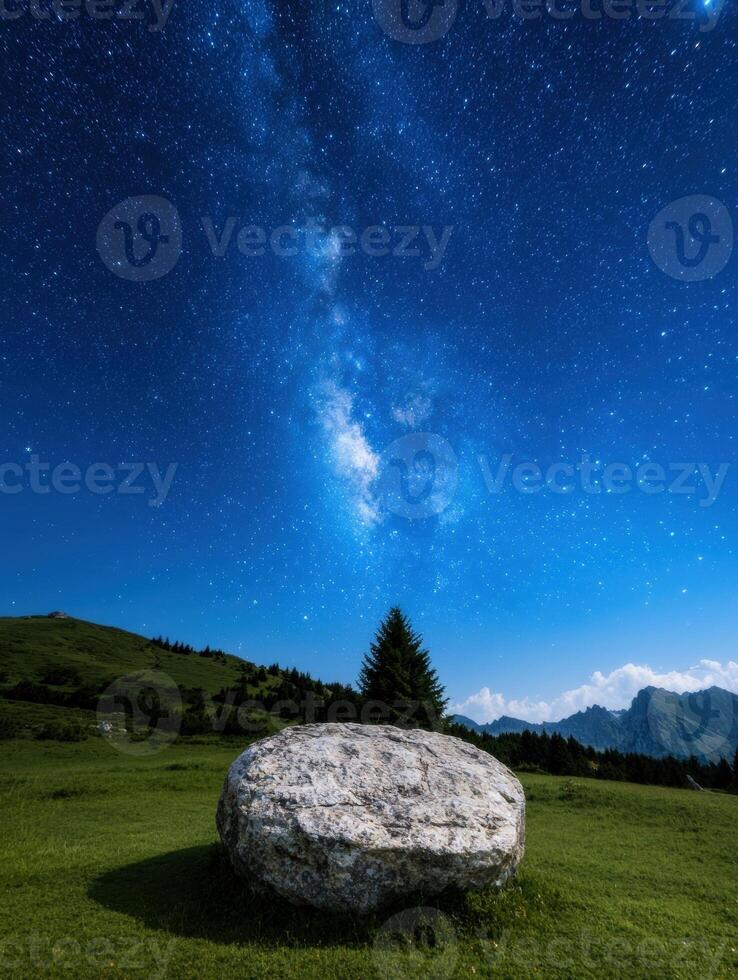 Milky way over a boulder in a grassy field at night photo
