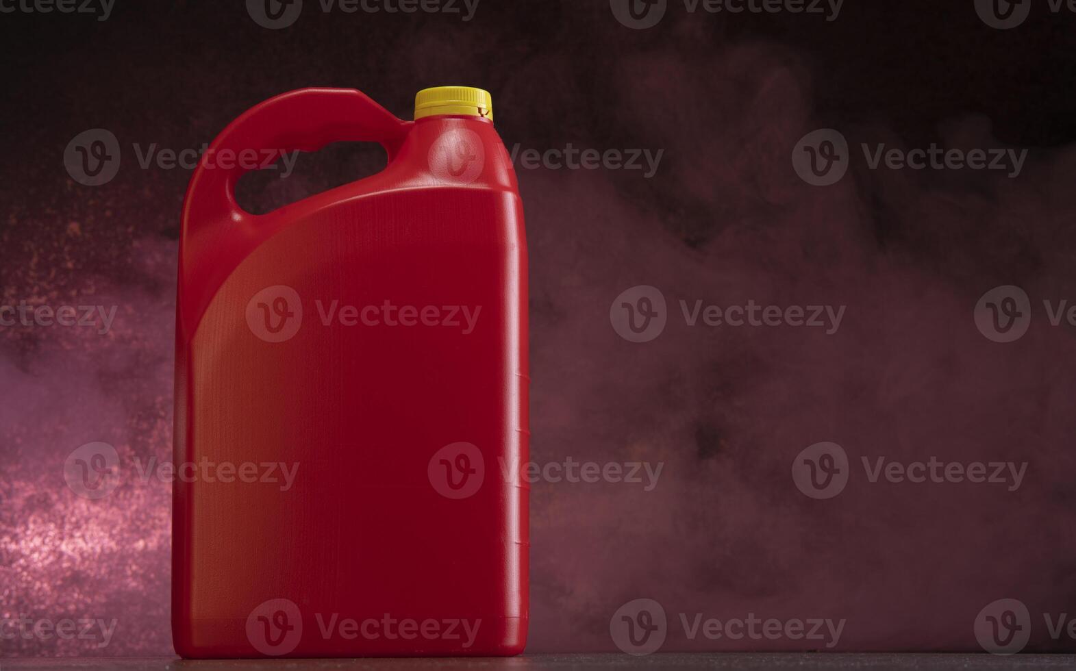 Front view of red plastic motor oil bottle, container with handle and yellow screw cap without label against dark background photo