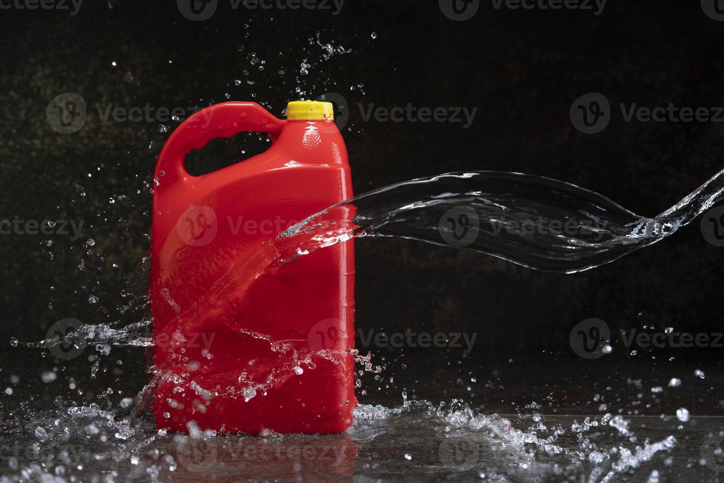Front view of red plastic motor oil bottle splashed by stream of water, container with handle and yellow screw cap without label photo