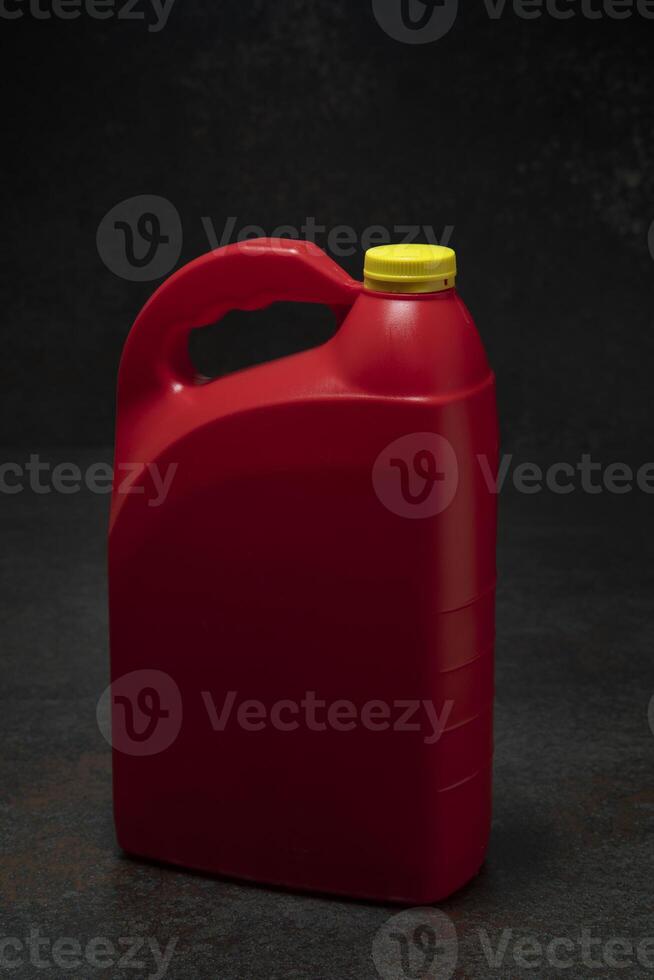 Three-quarter view of red plastic motor oil bottle with handle and yellow screw-top without label on dark ceramic photo