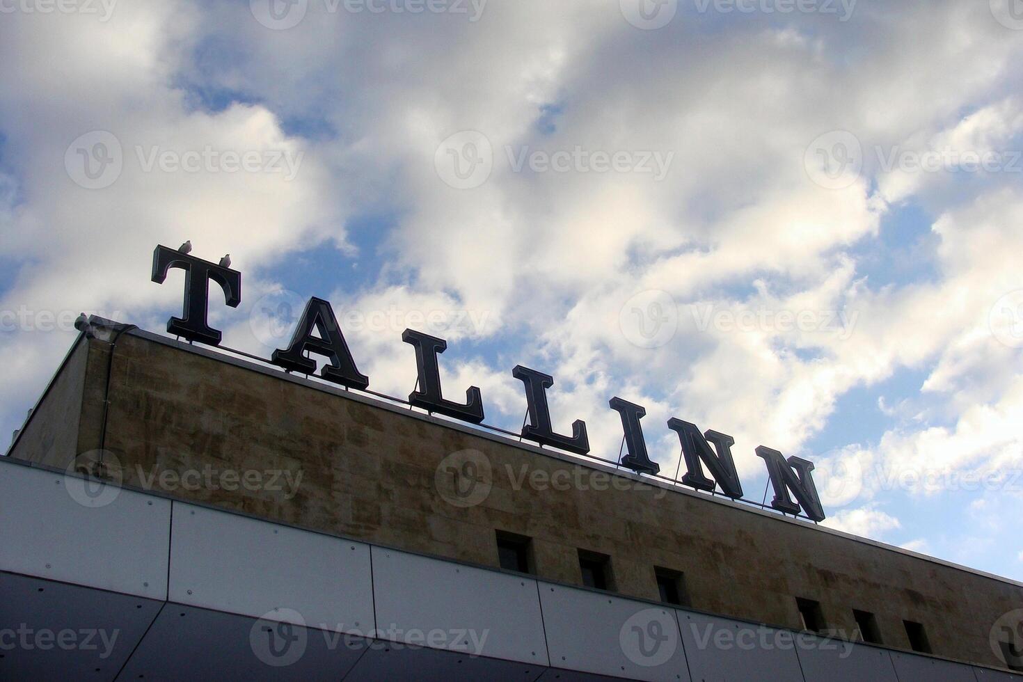 Low-angle shot of the Tallinn inscription on top of railway building. Close-up of the word Tallinn in large, bold letters on a building rooftop on an old building railway station against a cloudy sky photo
