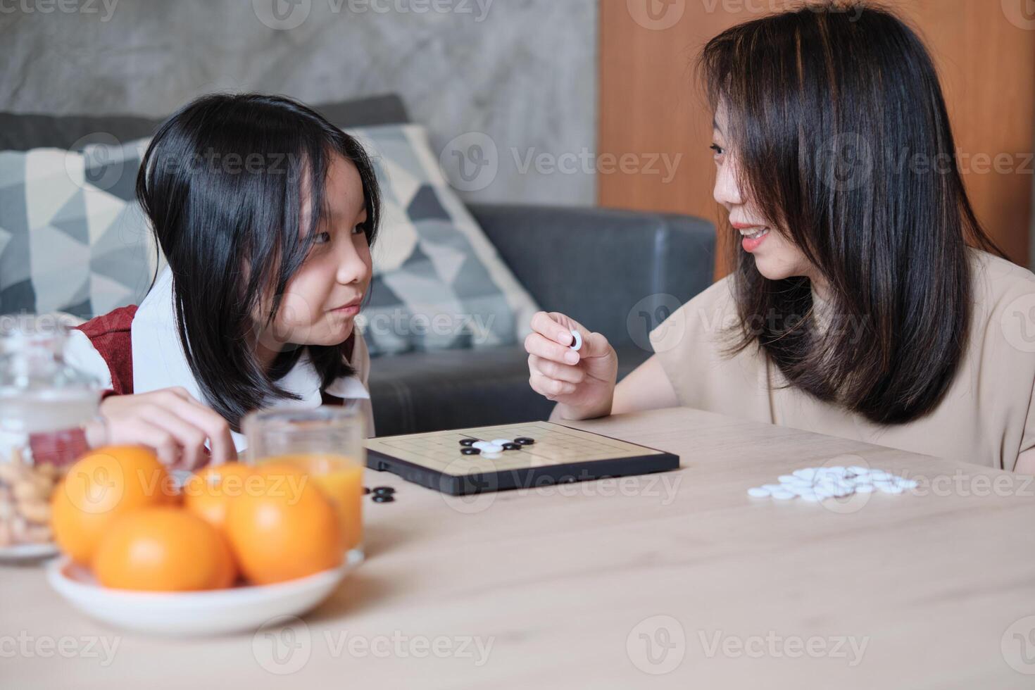 Asian family, mum, and kid fun playing Go game, checkers board on table in home living room together with love and cheerful, happy weekend relaxing hobby of child and parent, concentrate and compete. photo