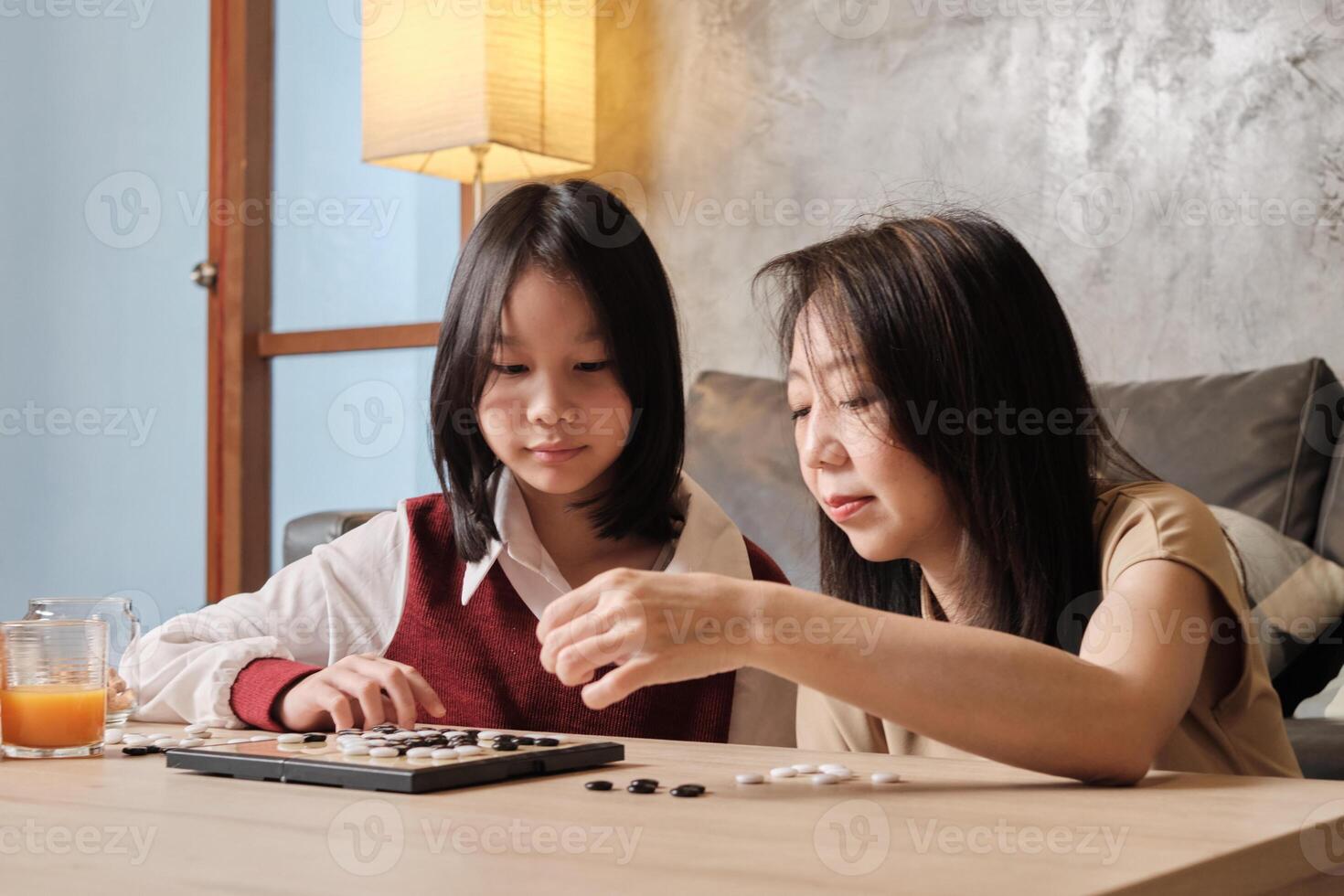 Asian family, mum, and kid playing Go, checkers board game on table in home living room together with love and relax, happy weekend hobby of child and parent, concentrate and compete. photo