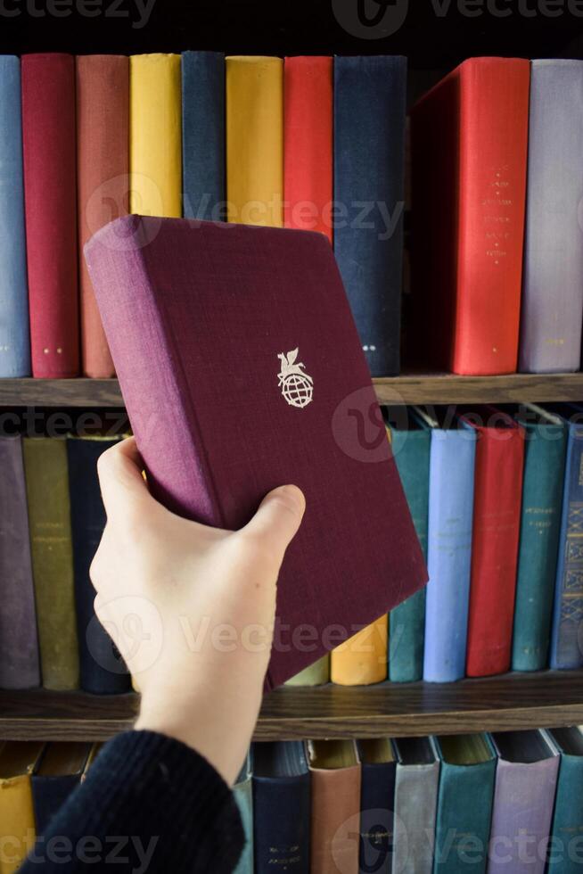 Book in hand. Bookshelf with different books. Library. photo