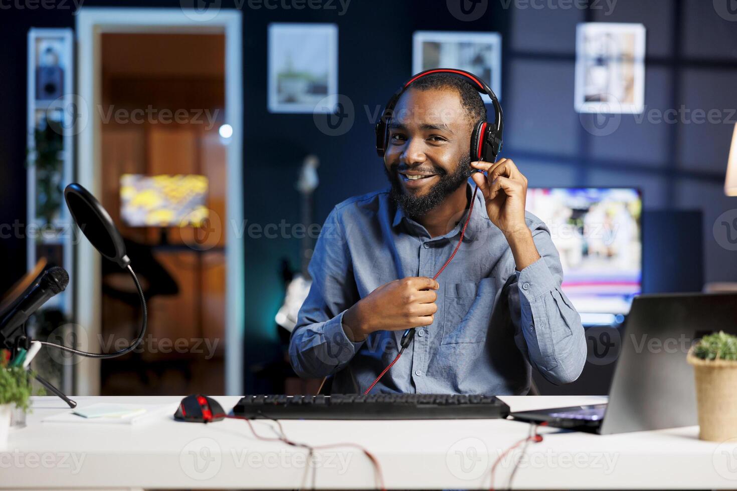 Cheerful BIPOC internet show host in studio uses camera to film wired headphones review, happy with crisp sound. Influencer satisfied by noise cancelling effect on stereo music listening device photo