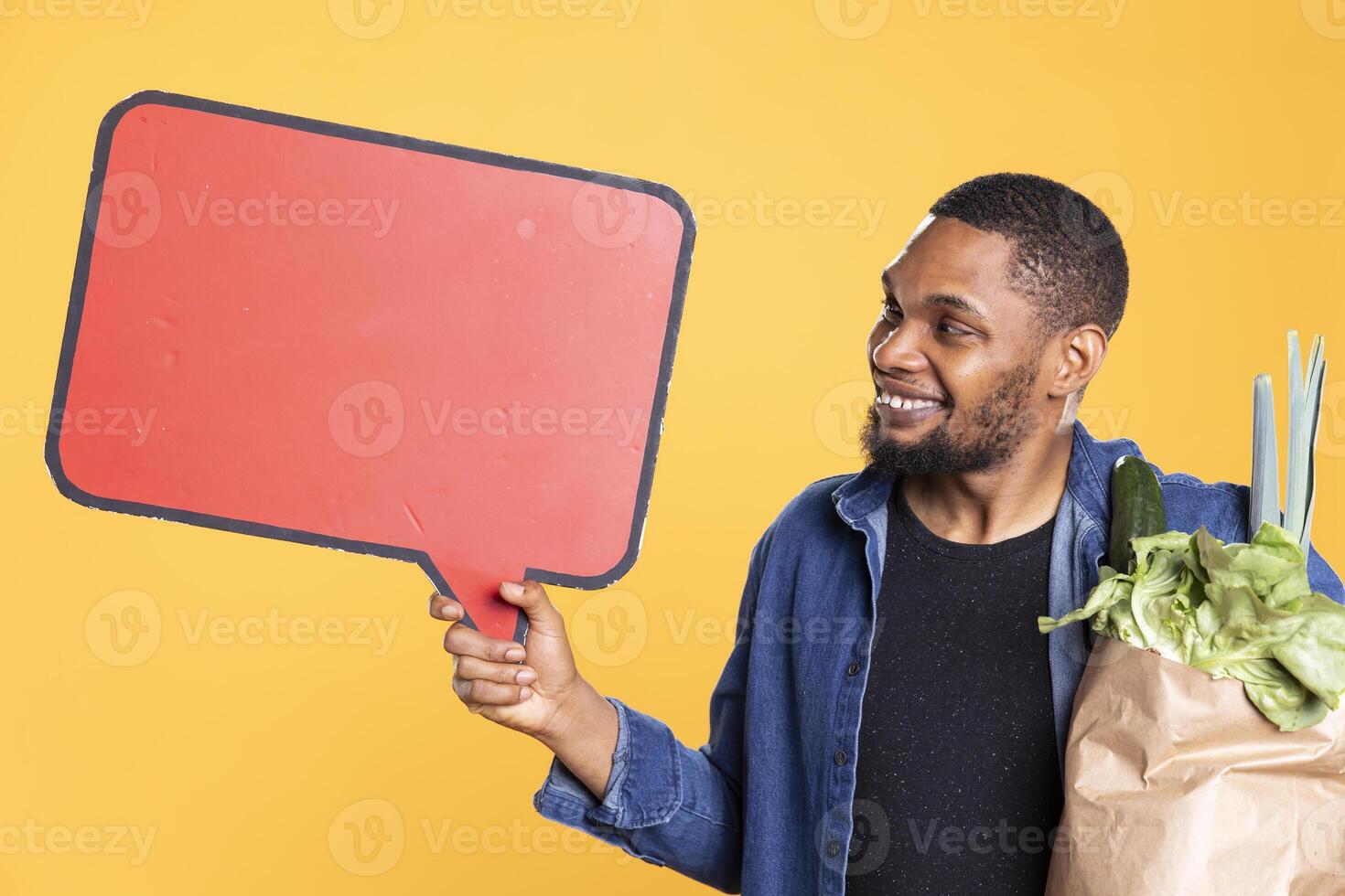 African american guy holds a speech bubble empty icon to create an ad for zero waste and sustainable lifestyle. Doing a promotional marketing advertisement for fresh bio fruits and veggies. photo
